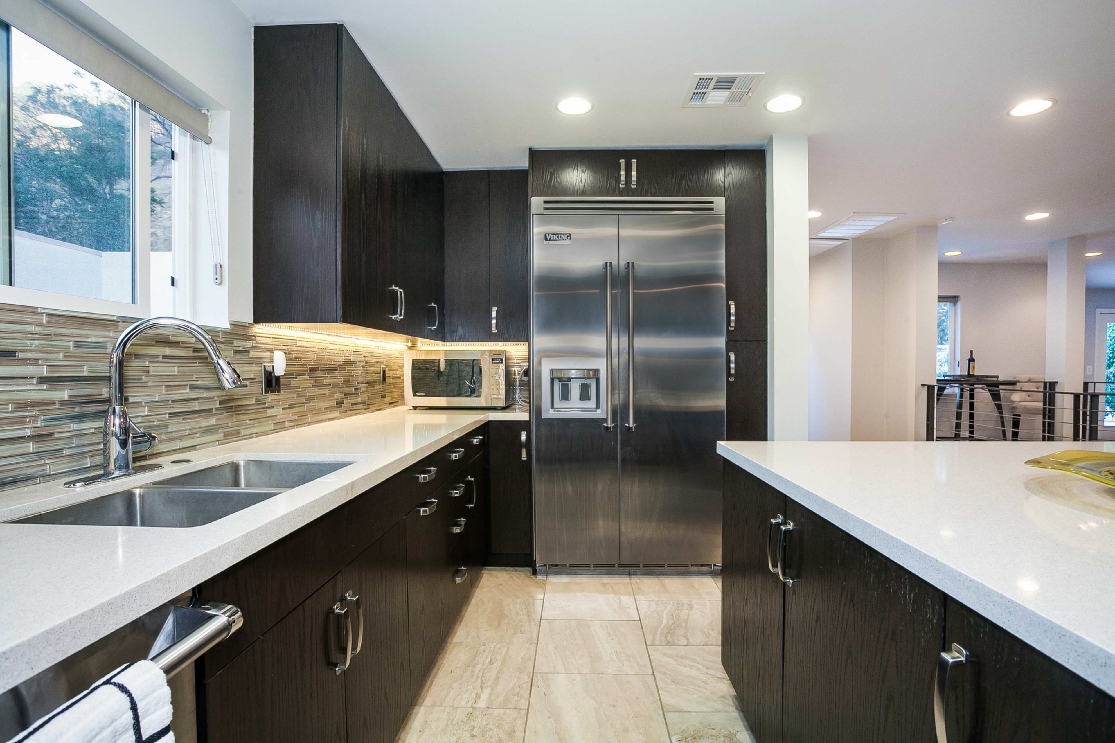 The image shows a modern kitchen with dark cabinets, stainless steel appliances, and a light-colored countertop.