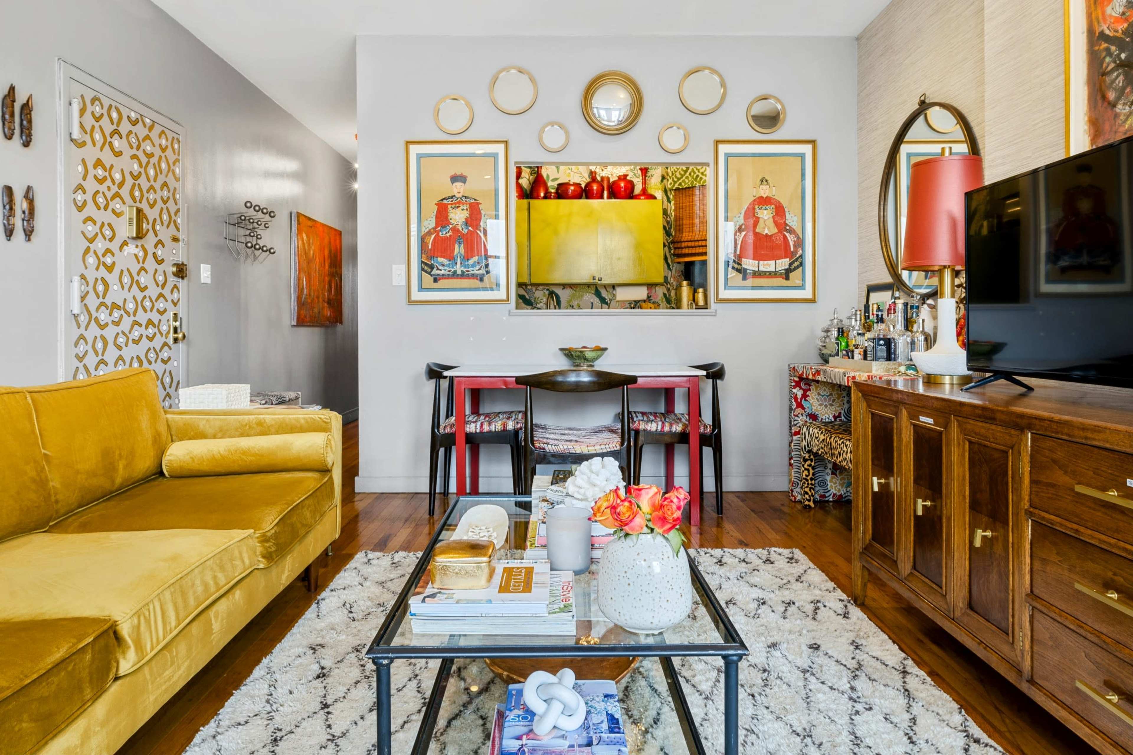 A cozy living room featuring a yellow sofa, a glass coffee table with decorative items, and a dining area with framed artwork on the walls.