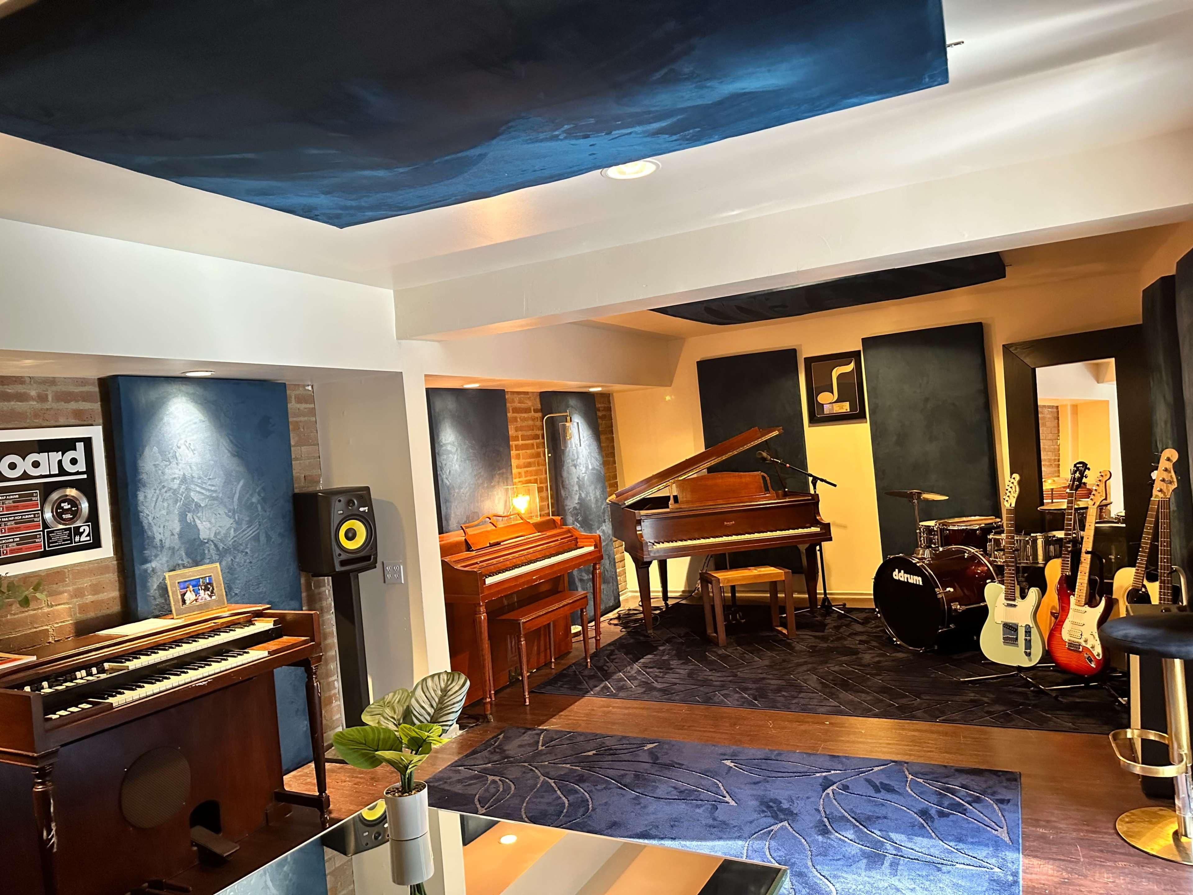 A music studio featuring a grand piano, an upright piano, various musical instruments, and soundproofed walls in a well-lit room.