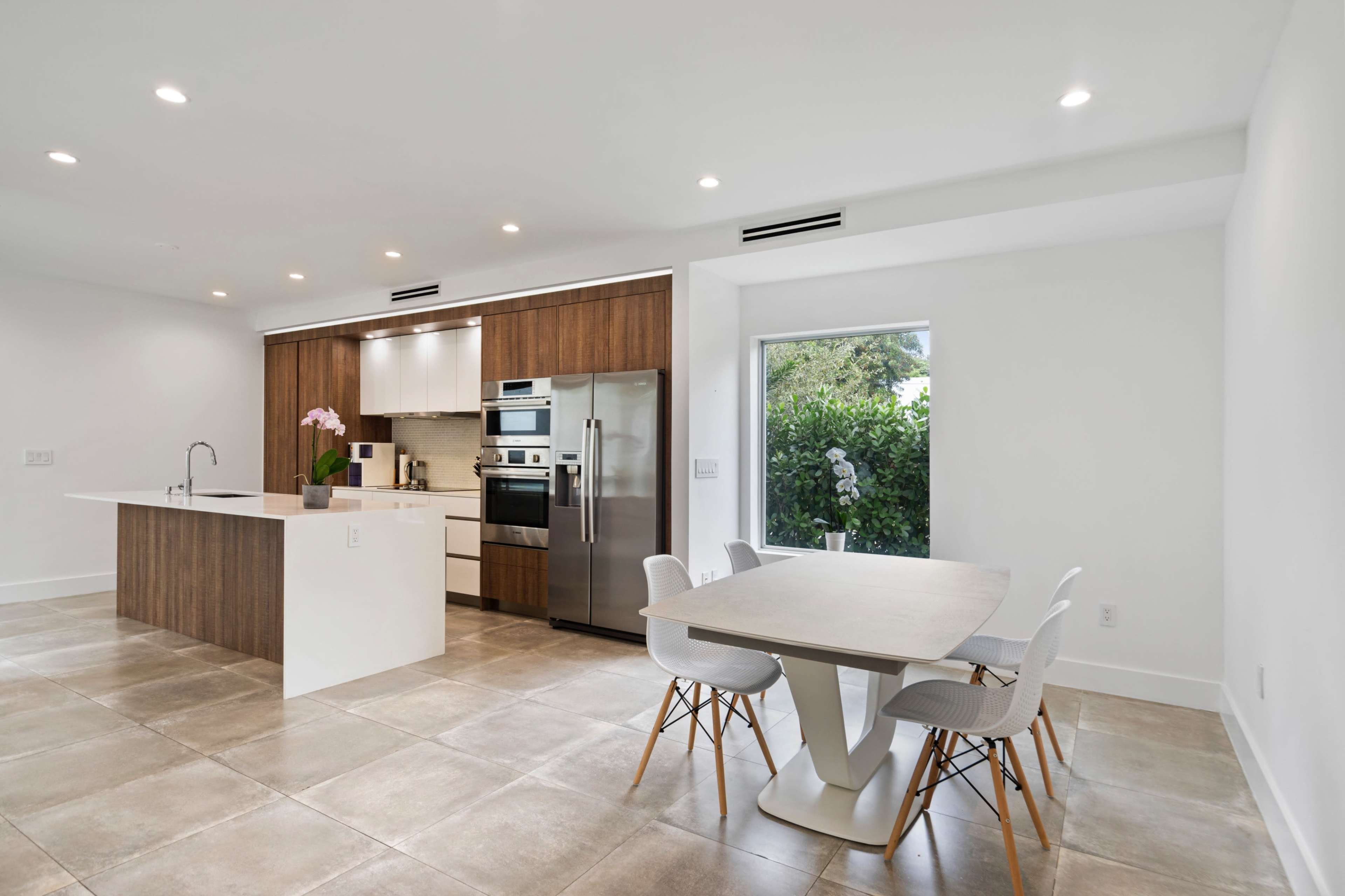 A modern kitchen features wooden cabinetry, stainless steel appliances, and a dining area with a minimalistic table and chairs.