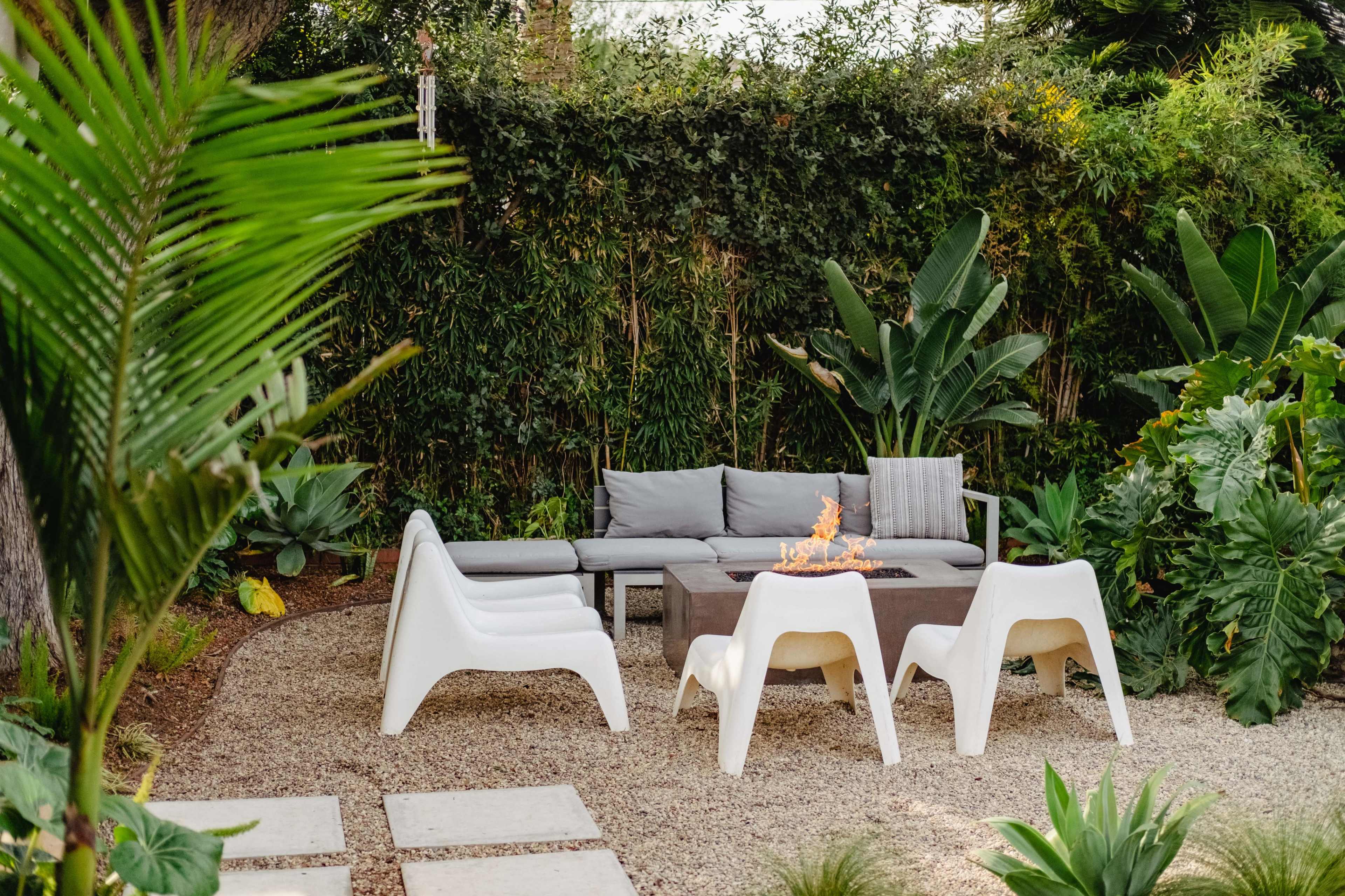 A seating area with a fire pit surrounded by modern white chairs and lush greenery in a garden.