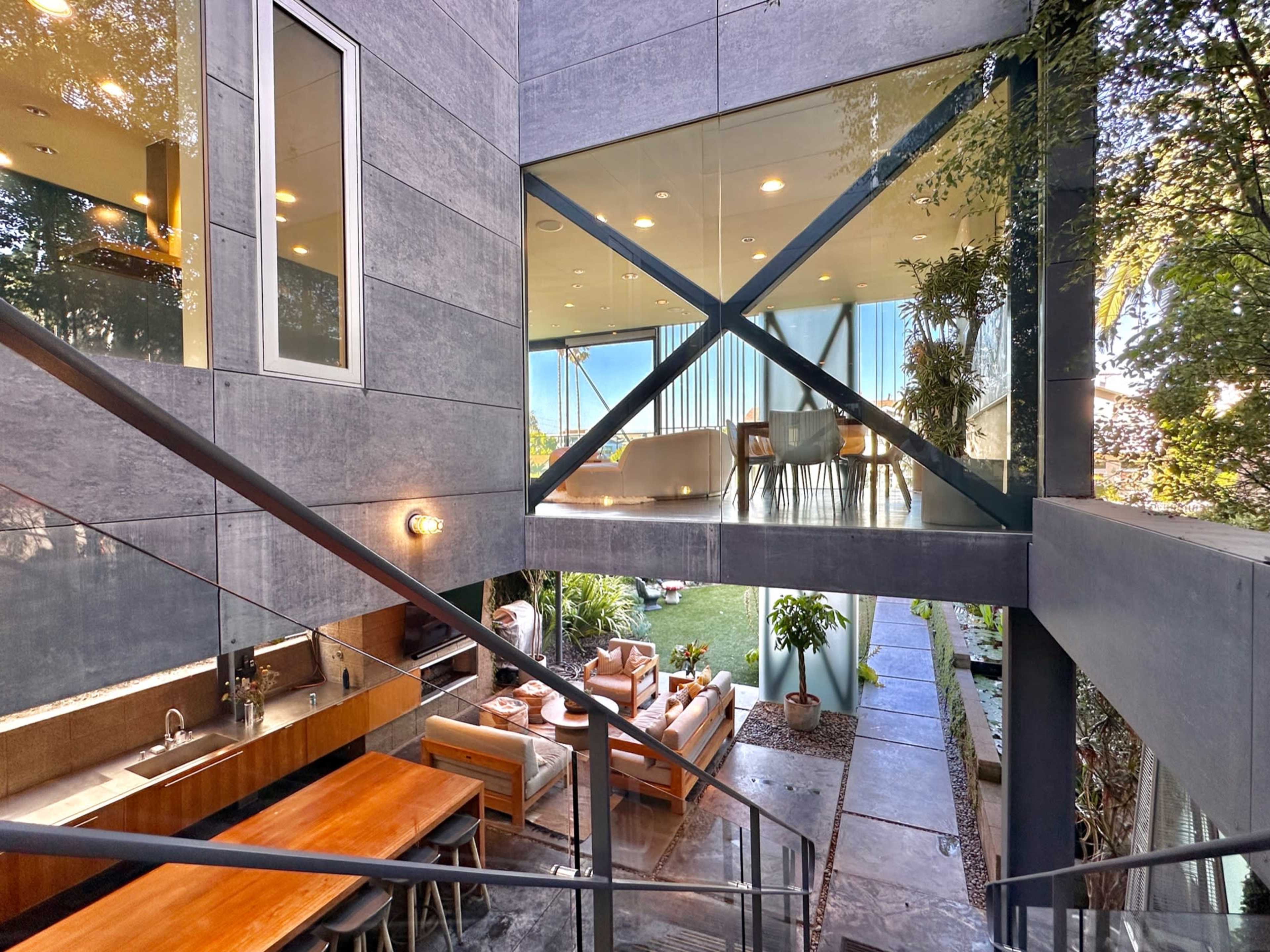 A modern multi-level home features an open kitchen and dining area on one floor, with expansive glass walls overlooking a landscaped garden below.