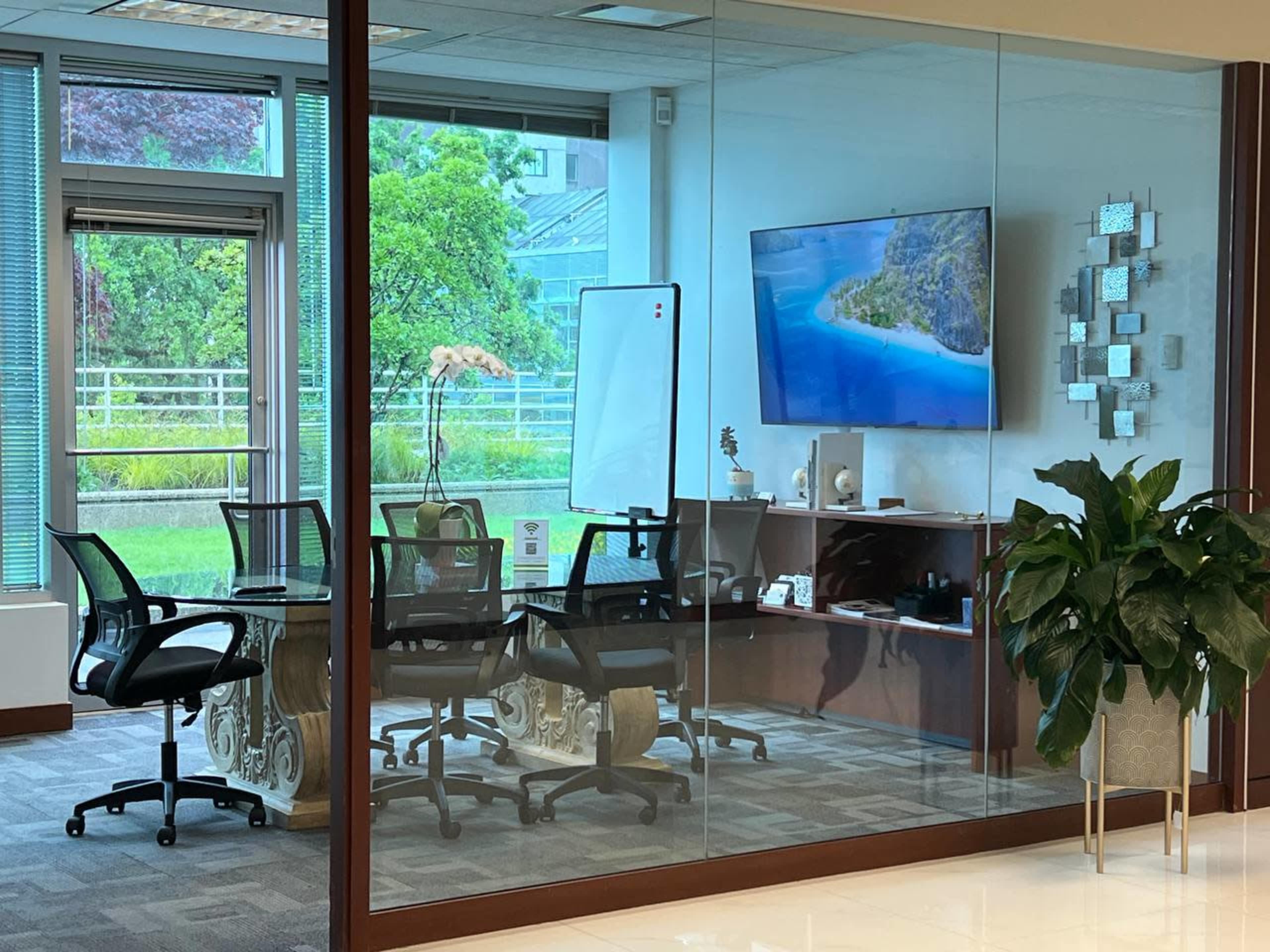 A modern conference room features glass walls, a large screen displaying a scenic image, and a round table surrounded by black chairs.