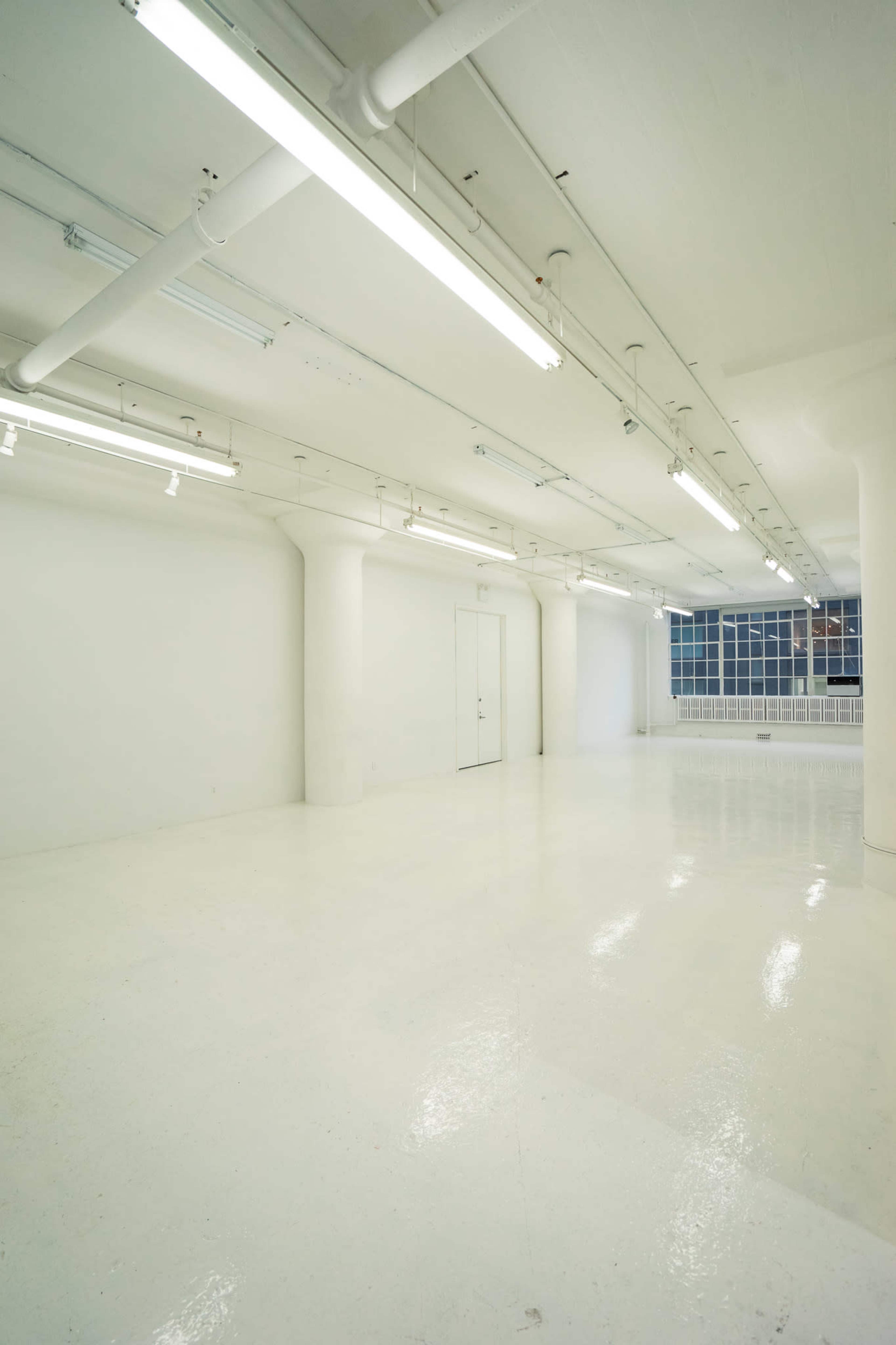 A spacious, empty white room with fluorescent lighting and large windows.