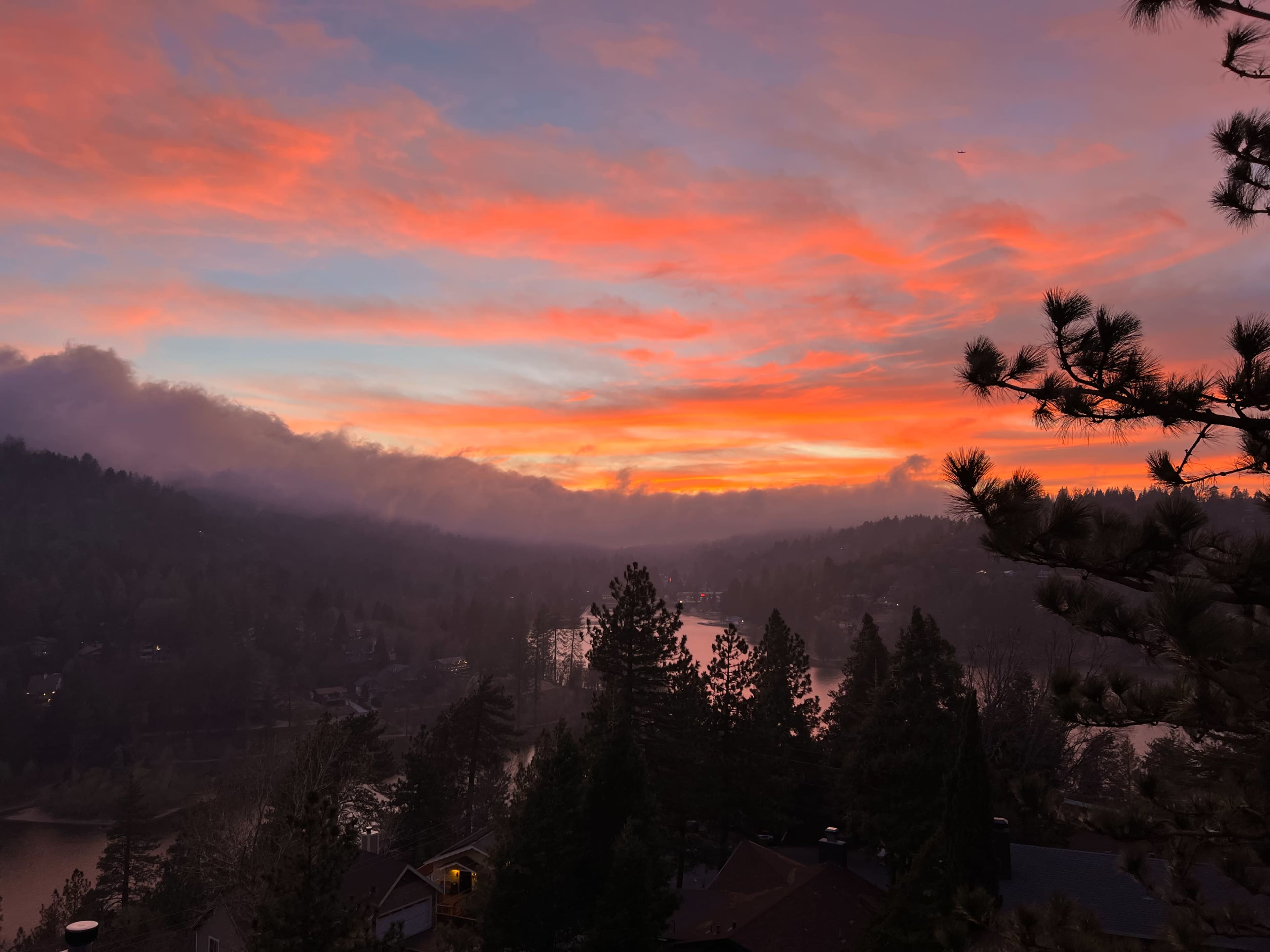 The scene features a vibrant sunset over a forested valley with a winding river, framed by silhouettes of trees.