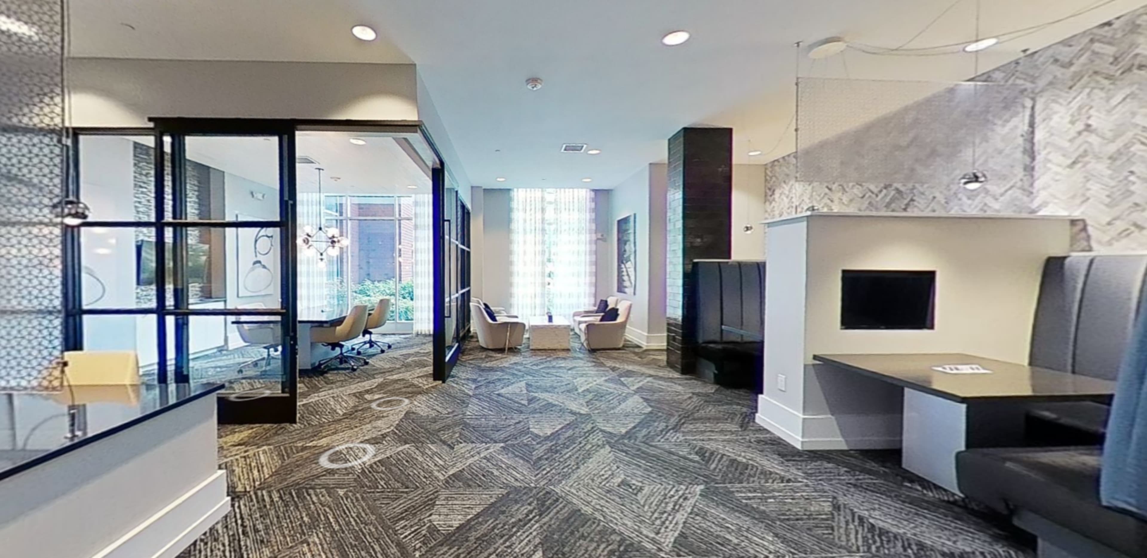 A modern lobby area featuring seating arrangements, a TV, and large windows allowing natural light to enter the space.