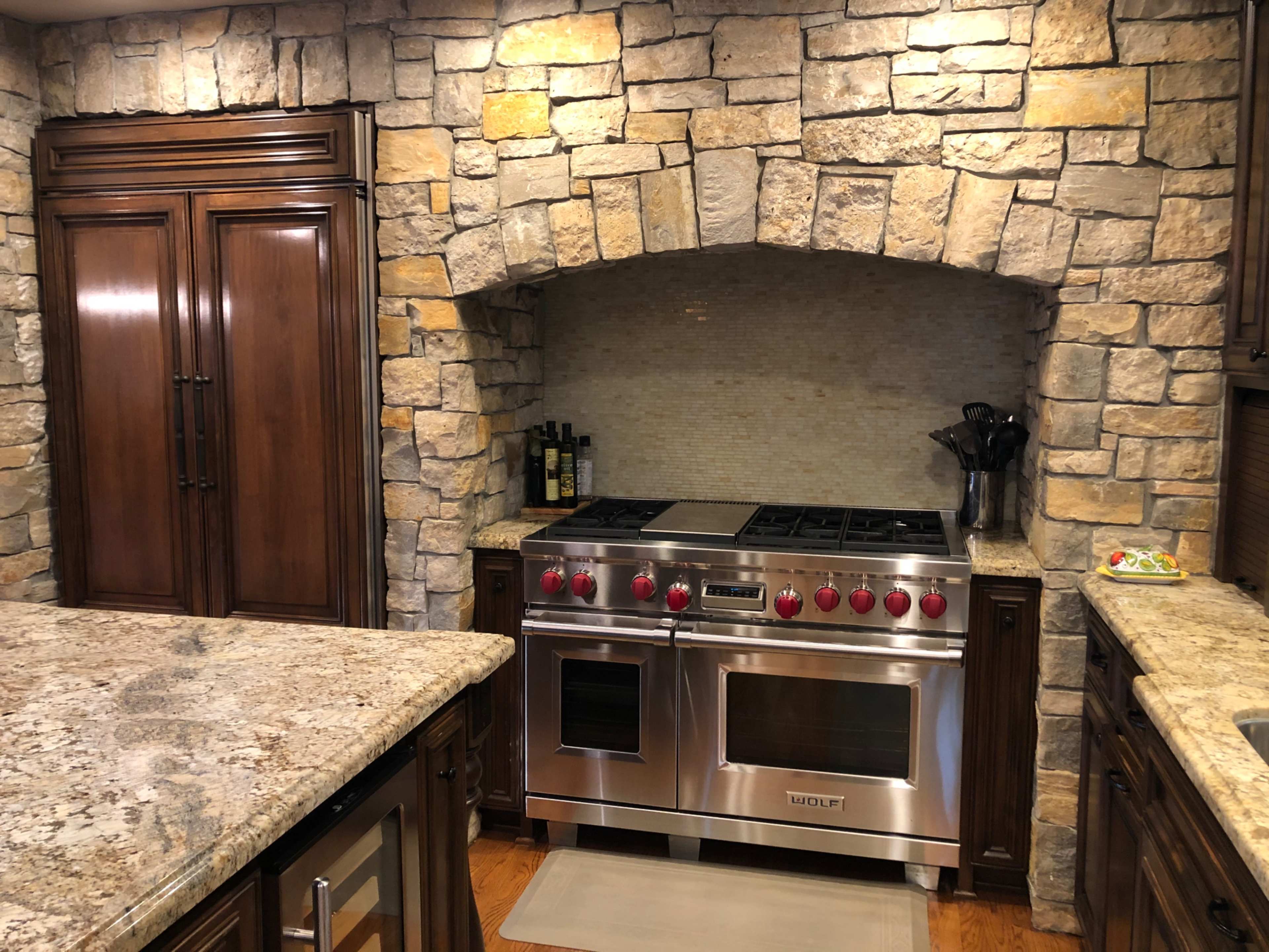 A kitchen featuring a stainless steel range with red knobs, set against a rustic stone arch and dark wood cabinetry.