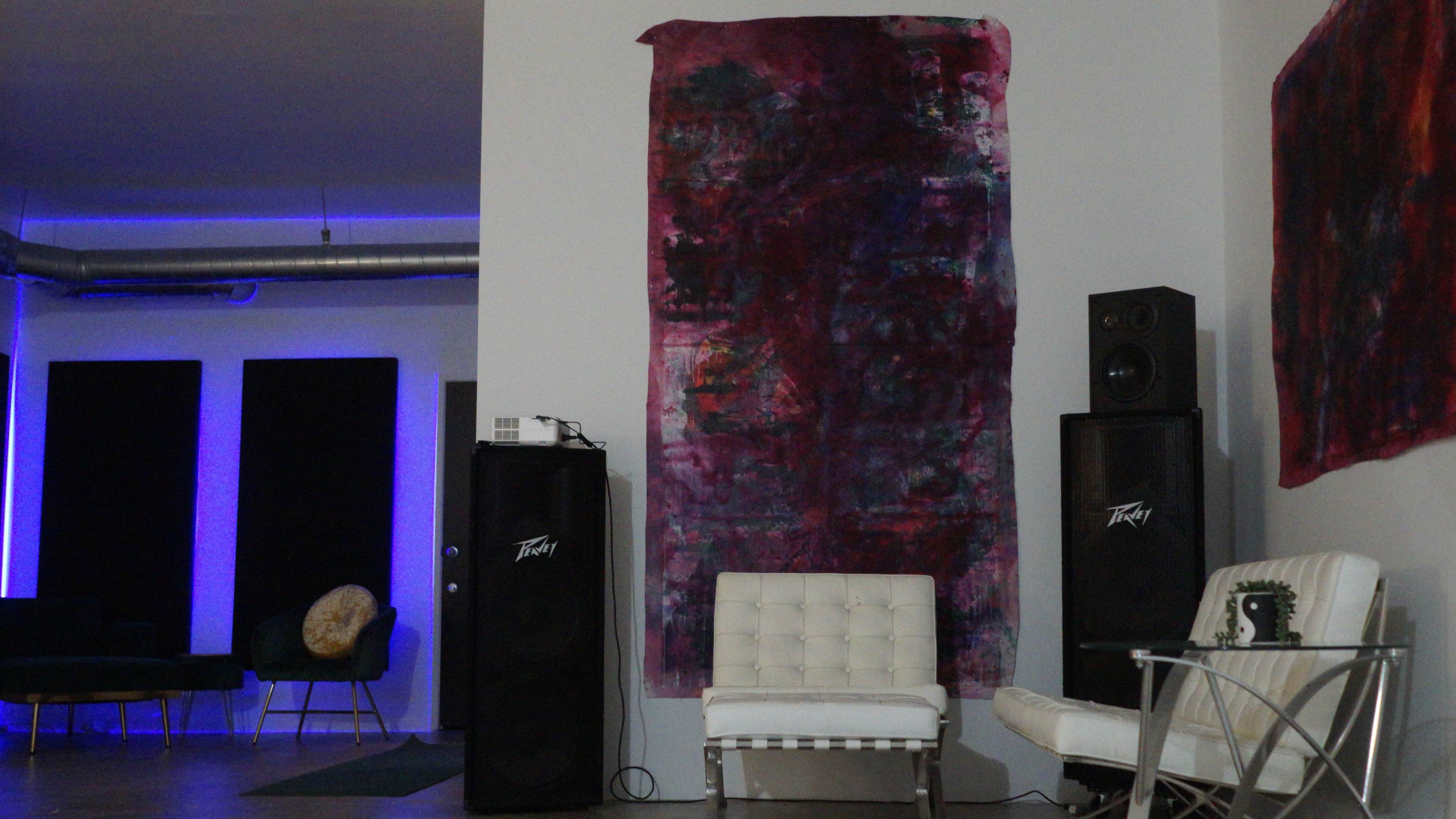 A modern interior space featuring a white chair, large speakers, and a colorful abstract painting on the wall.