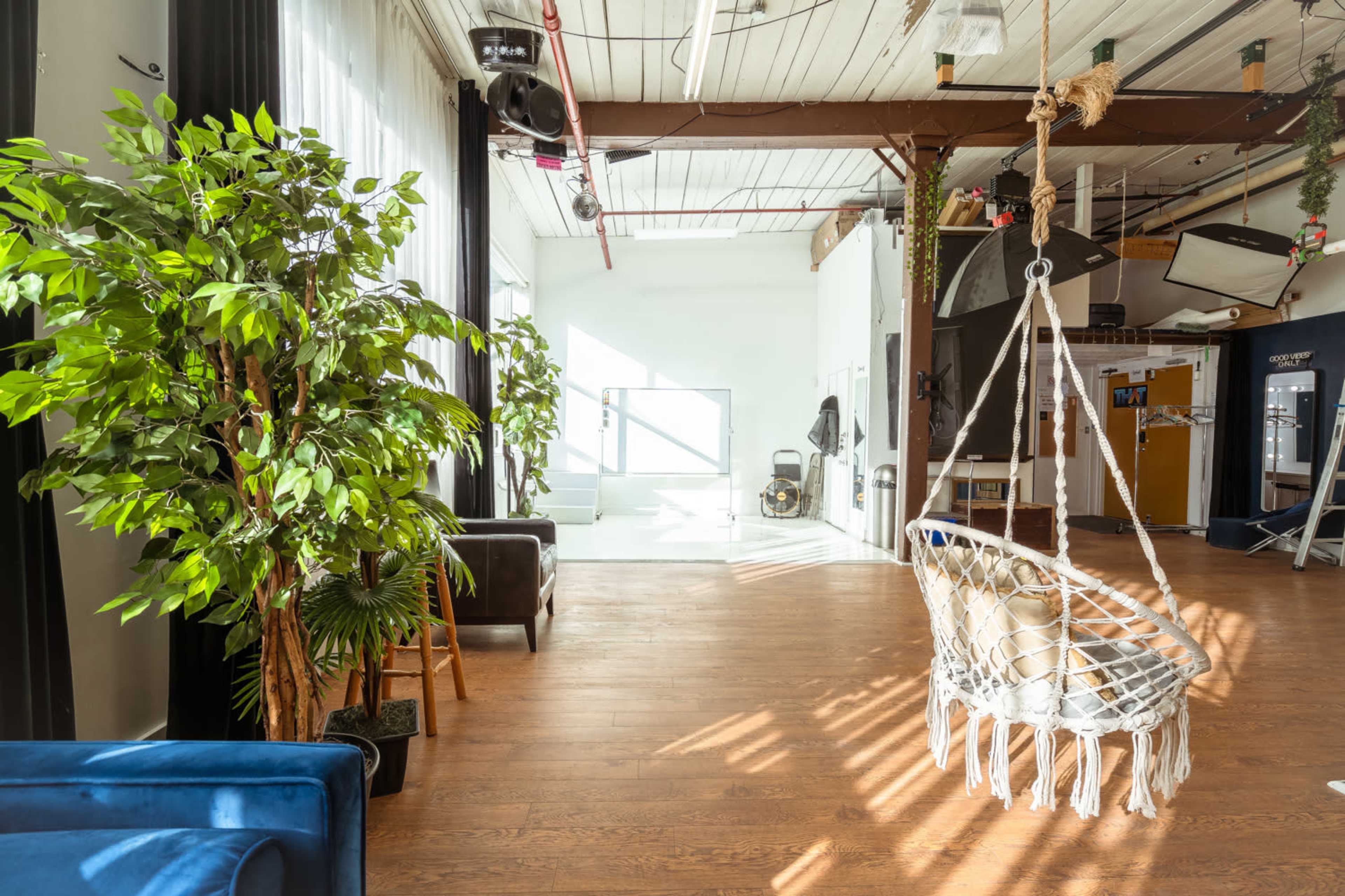 A spacious interior featuring a hanging macramé chair, potted plants, and large windows that allow natural light to fill the room.