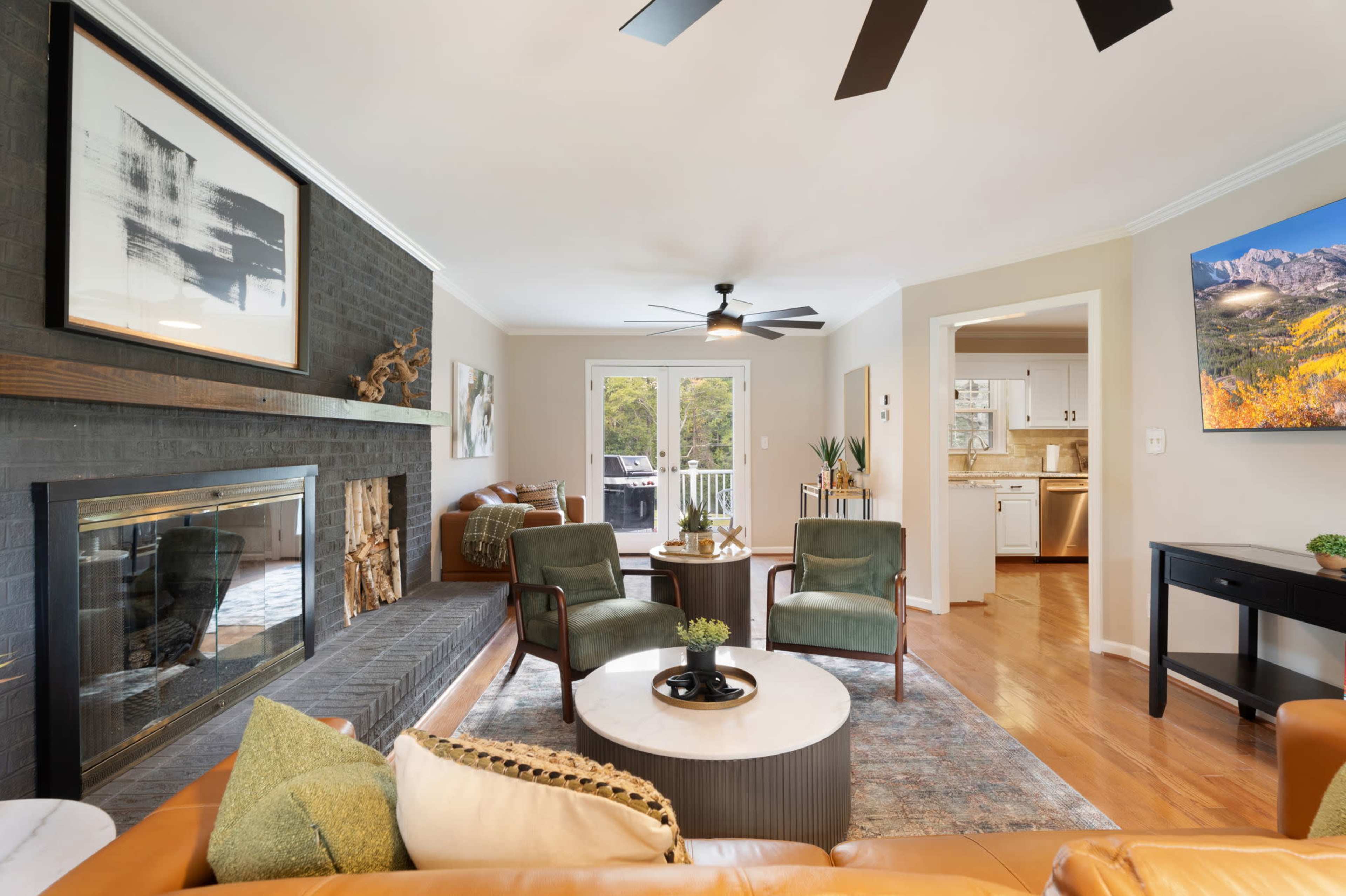 The living room features a black brick fireplace, two green chairs, a round coffee table, and a view into a kitchen area with light cabinetry.
