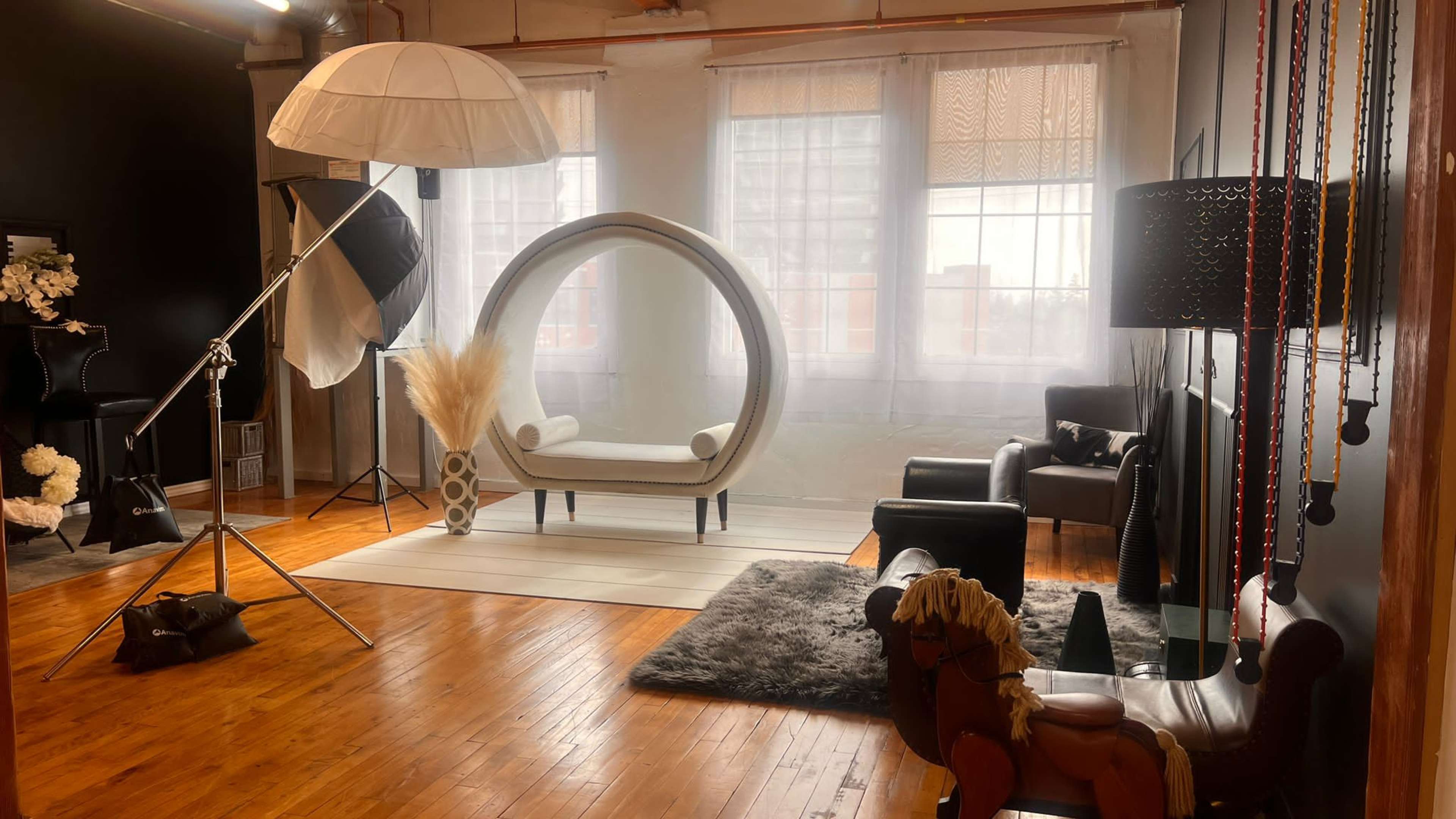 A stylish photo studio interior featuring a modern circular chair, soft lighting equipment, and a variety of seating arrangements on wooden flooring.