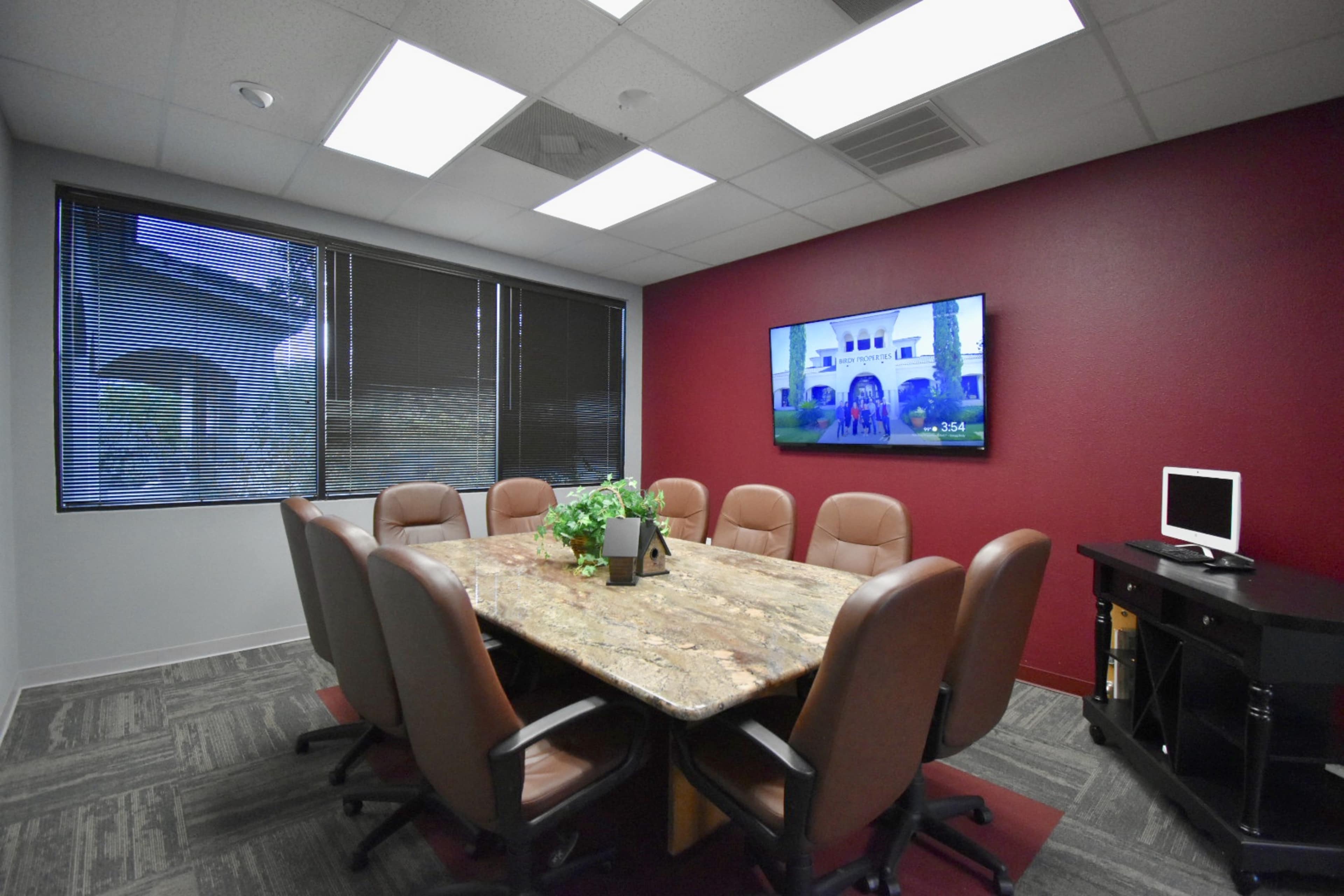 A conference room with a large stone table surrounded by leather chairs and a screen displaying an image on the wall.
