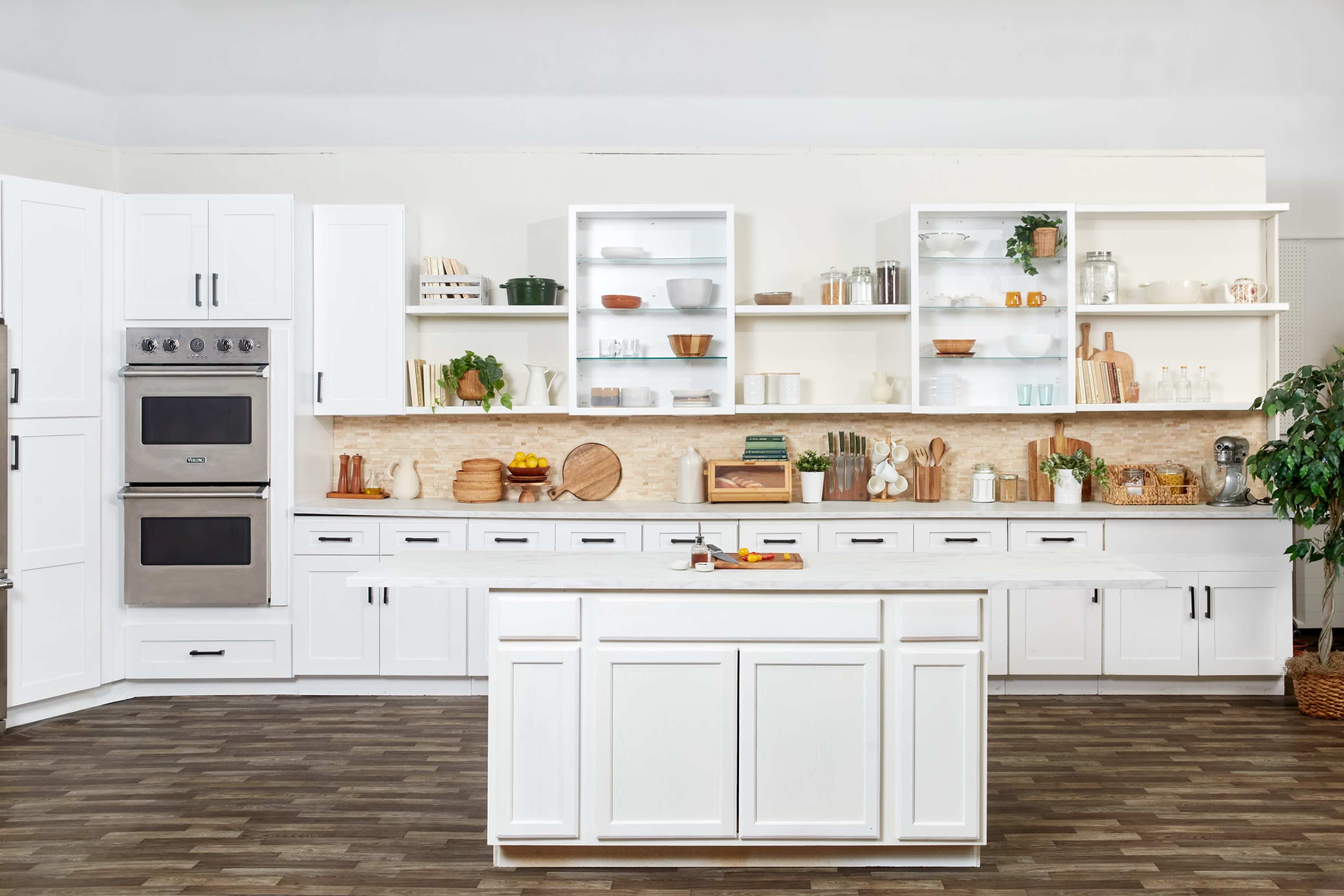 A modern kitchen features white cabinetry, a central island, and open shelves displaying various dishes and wooden kitchenware.