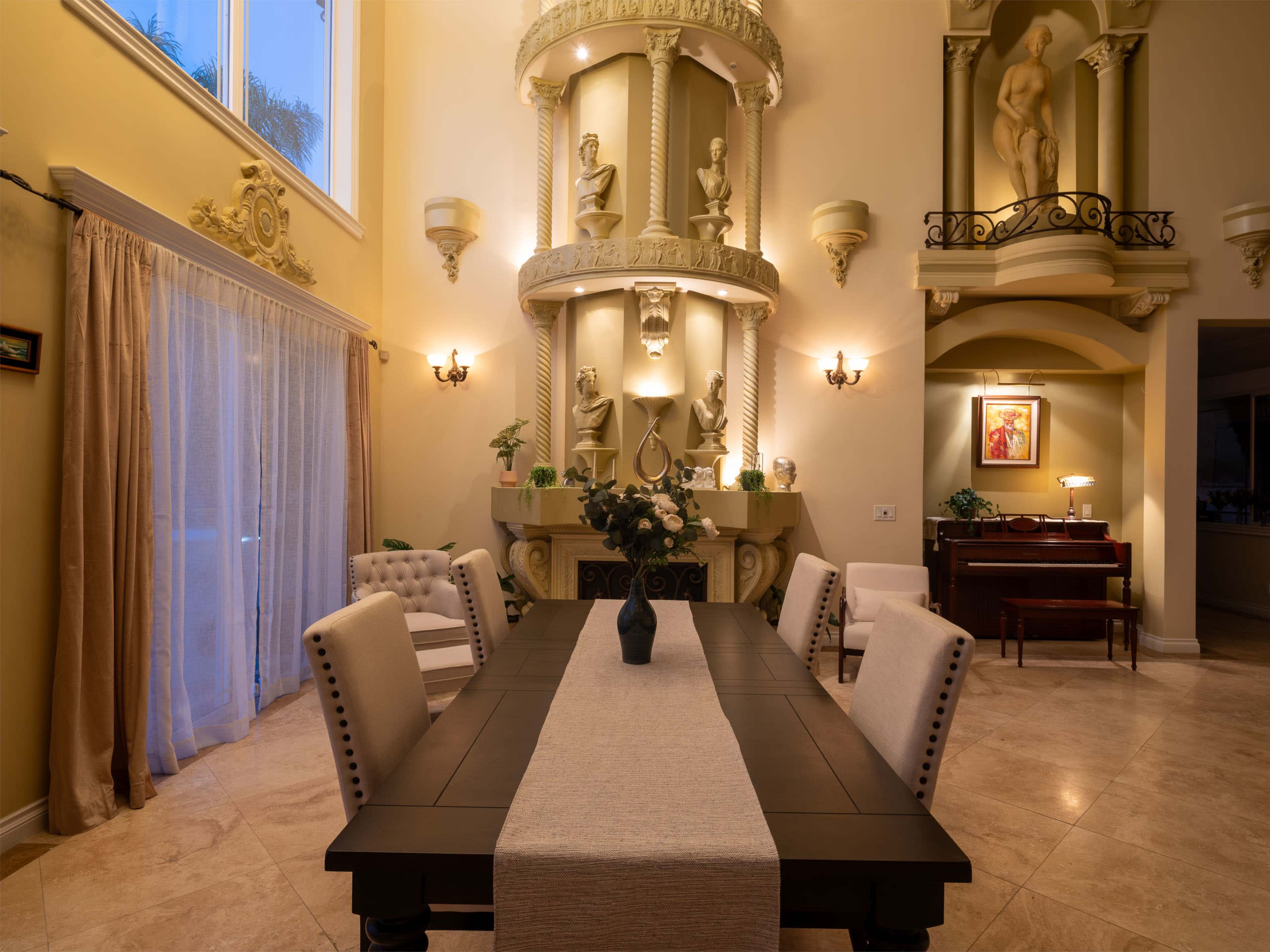 The image shows a spacious dining room with a large table set for six, flanked by elegant chairs and highlighted by architectural features and decorative sculptures on the walls.