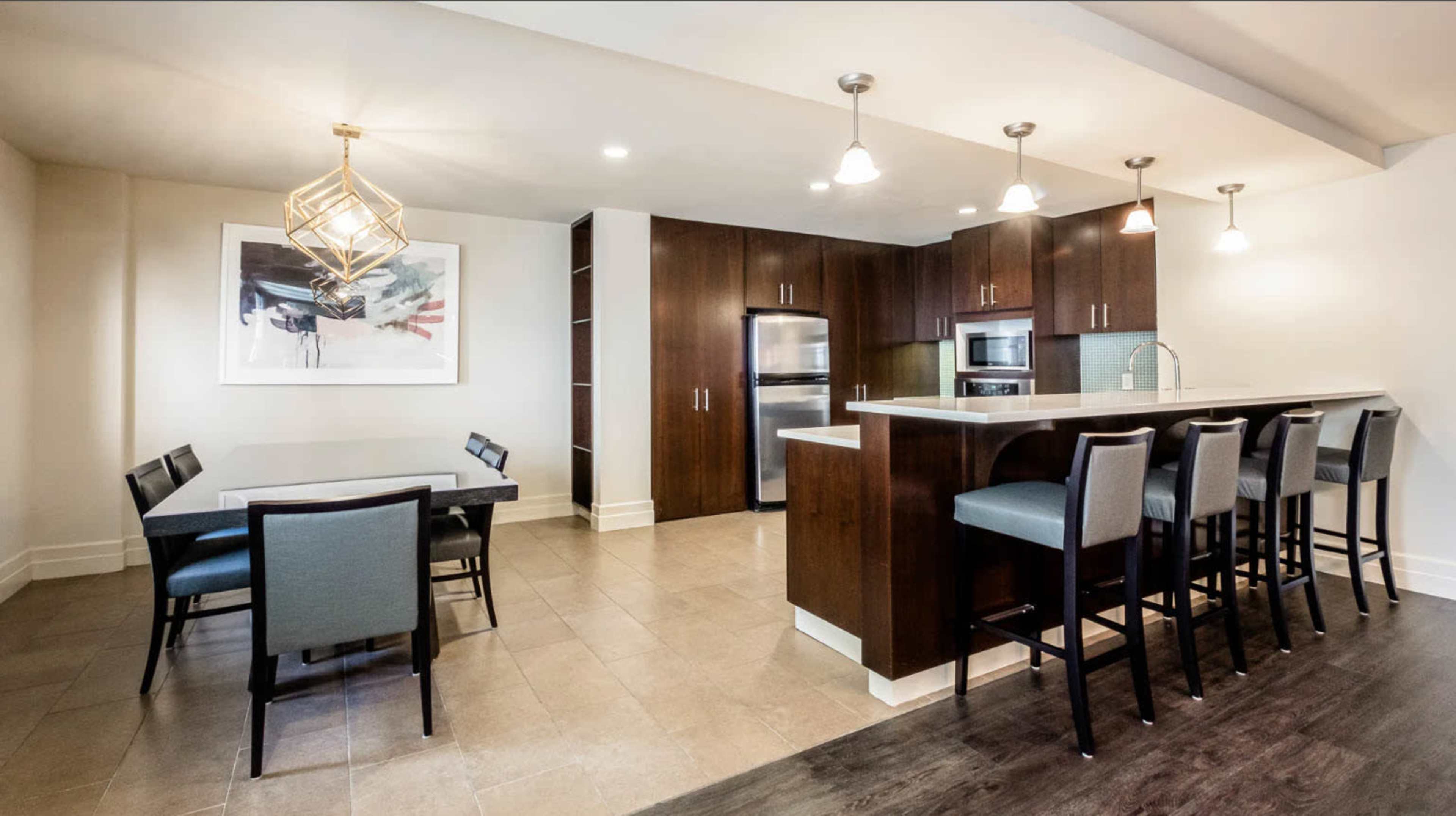 A modern kitchen and dining area featuring dark wood cabinetry, stainless steel appliances, a table with chairs, and bar seating at a kitchen counter.