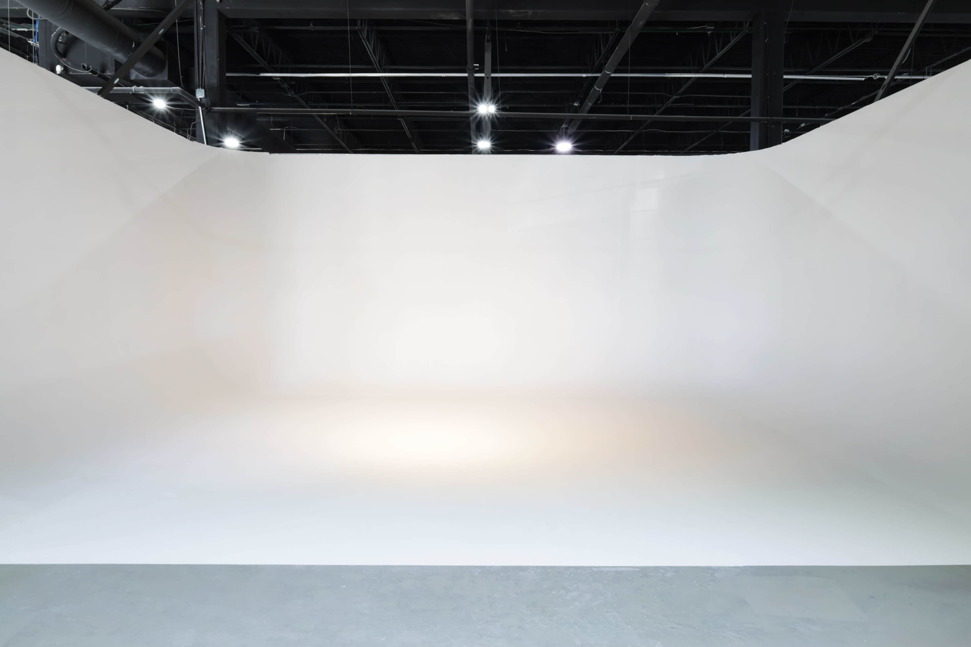 The image shows a spacious, empty studio with a white curved backdrop and soft lighting.