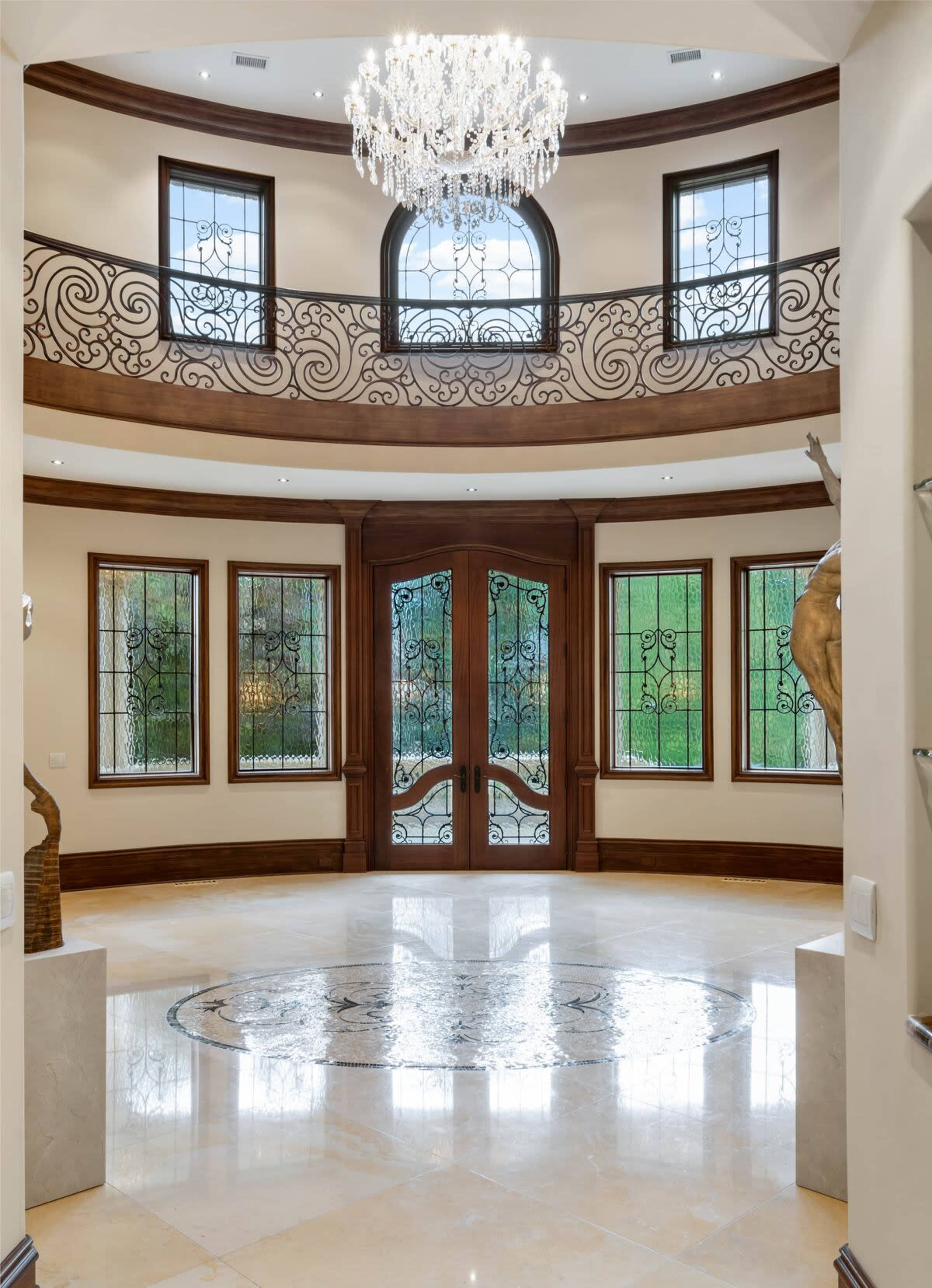 The entrance hall features a large chandelier, ornate railings, and decorative stained glass windows flanking double front doors.