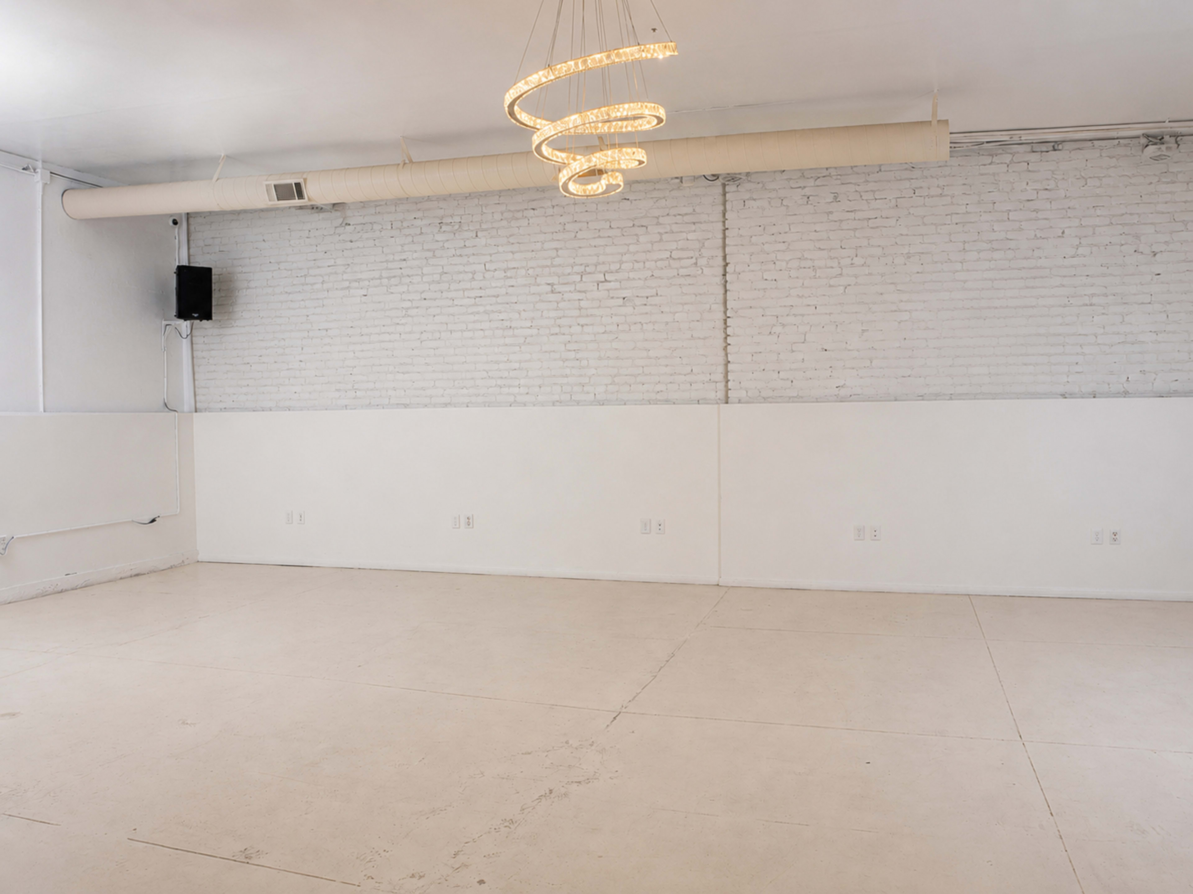 The image shows an empty room with white brick walls, a light fixture hanging from the ceiling, and a concrete floor.