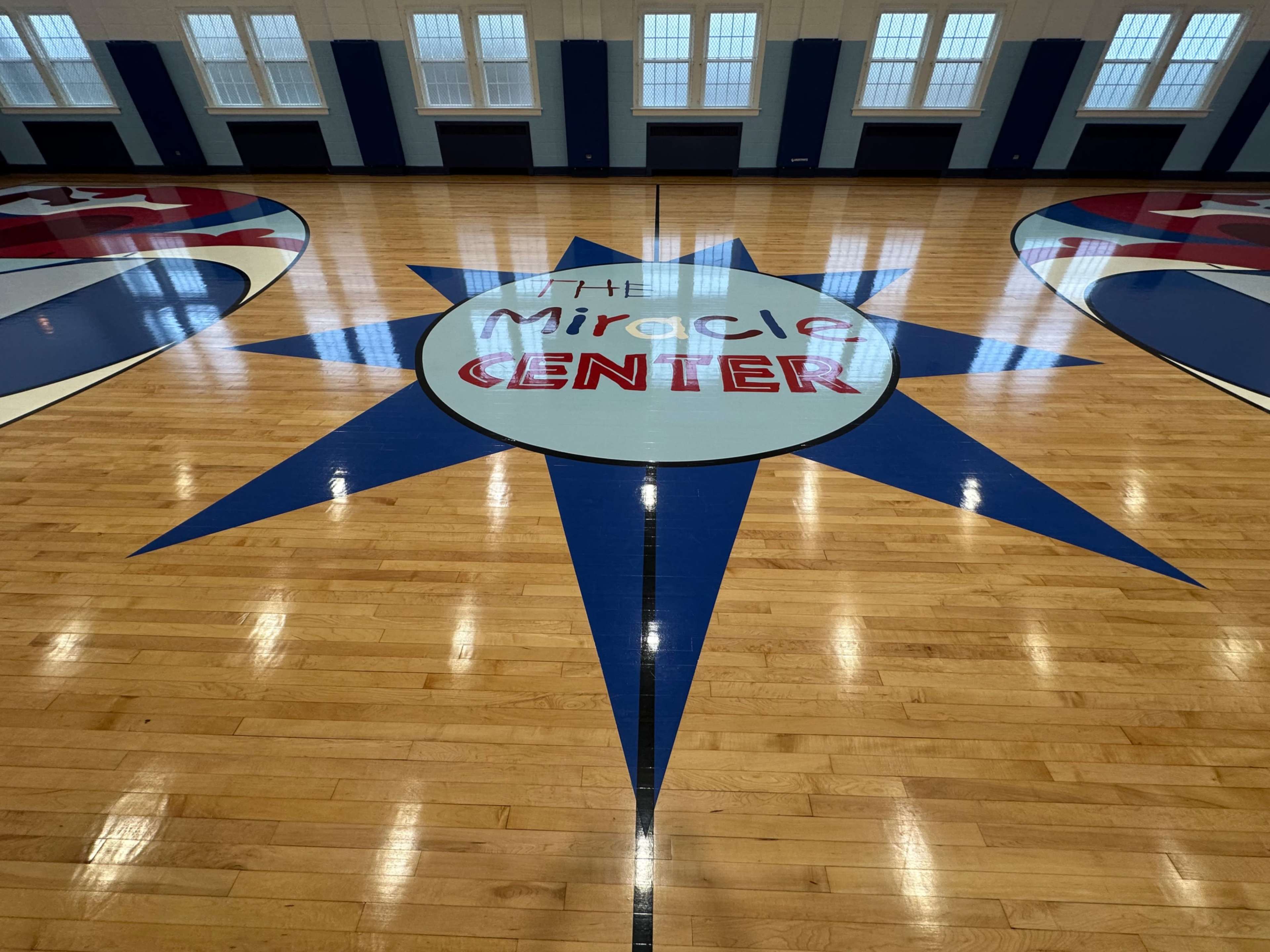 The image shows a gymnasium floor featuring a large star design with the words "The Miracle Center" in the center.