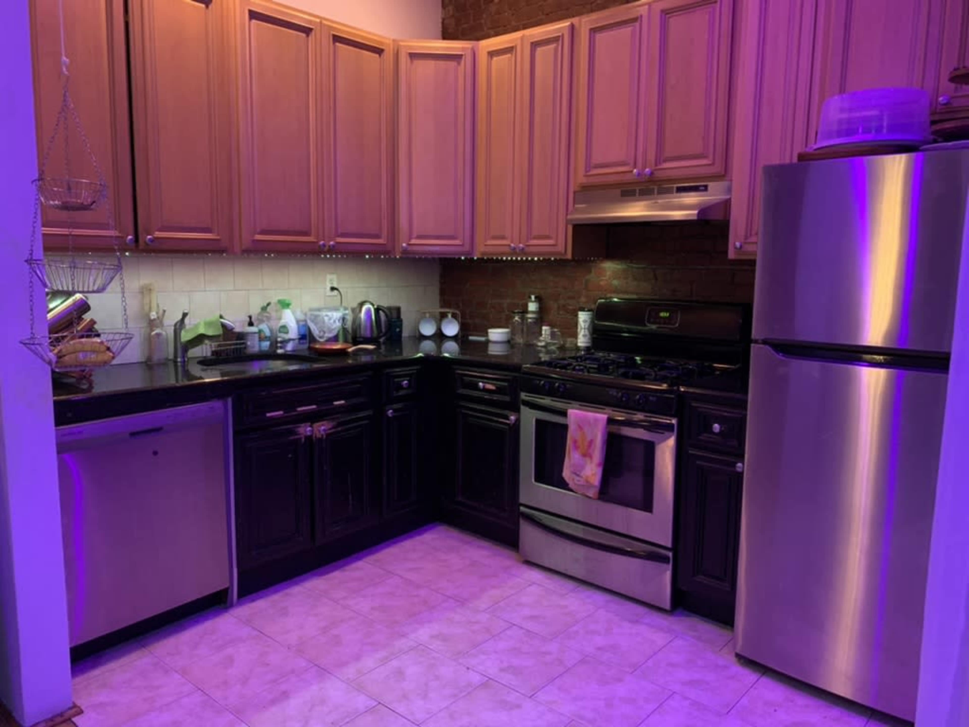 The kitchen features wooden cabinets, stainless steel appliances, and tiled flooring, illuminated by purple lighting.