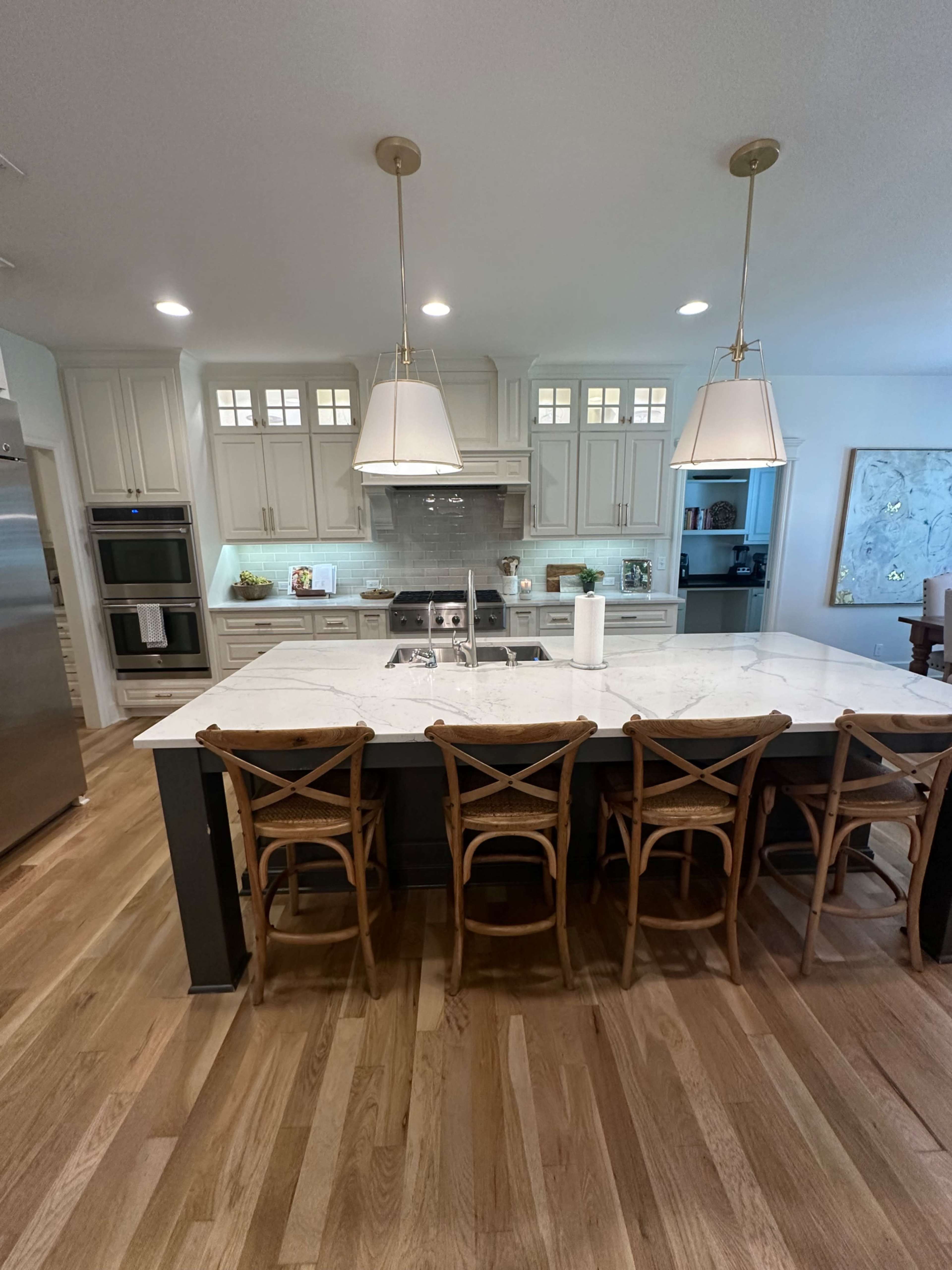 A modern kitchen with an island featuring a marble countertop, three wooden chairs, and pendant lighting.