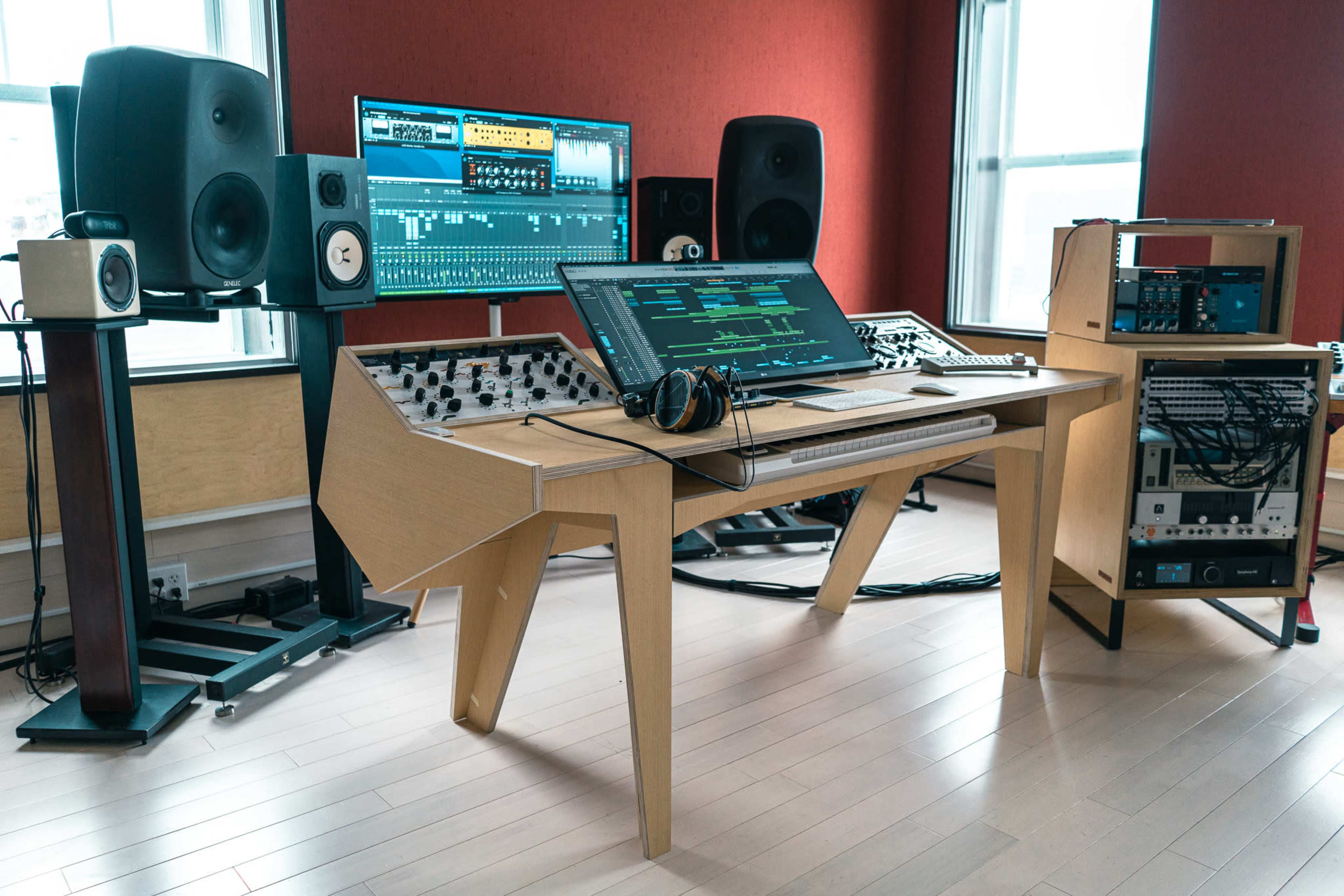 A modern music studio featuring a wooden workstation with a computer monitor, audio equipment, and speakers against a red wall.