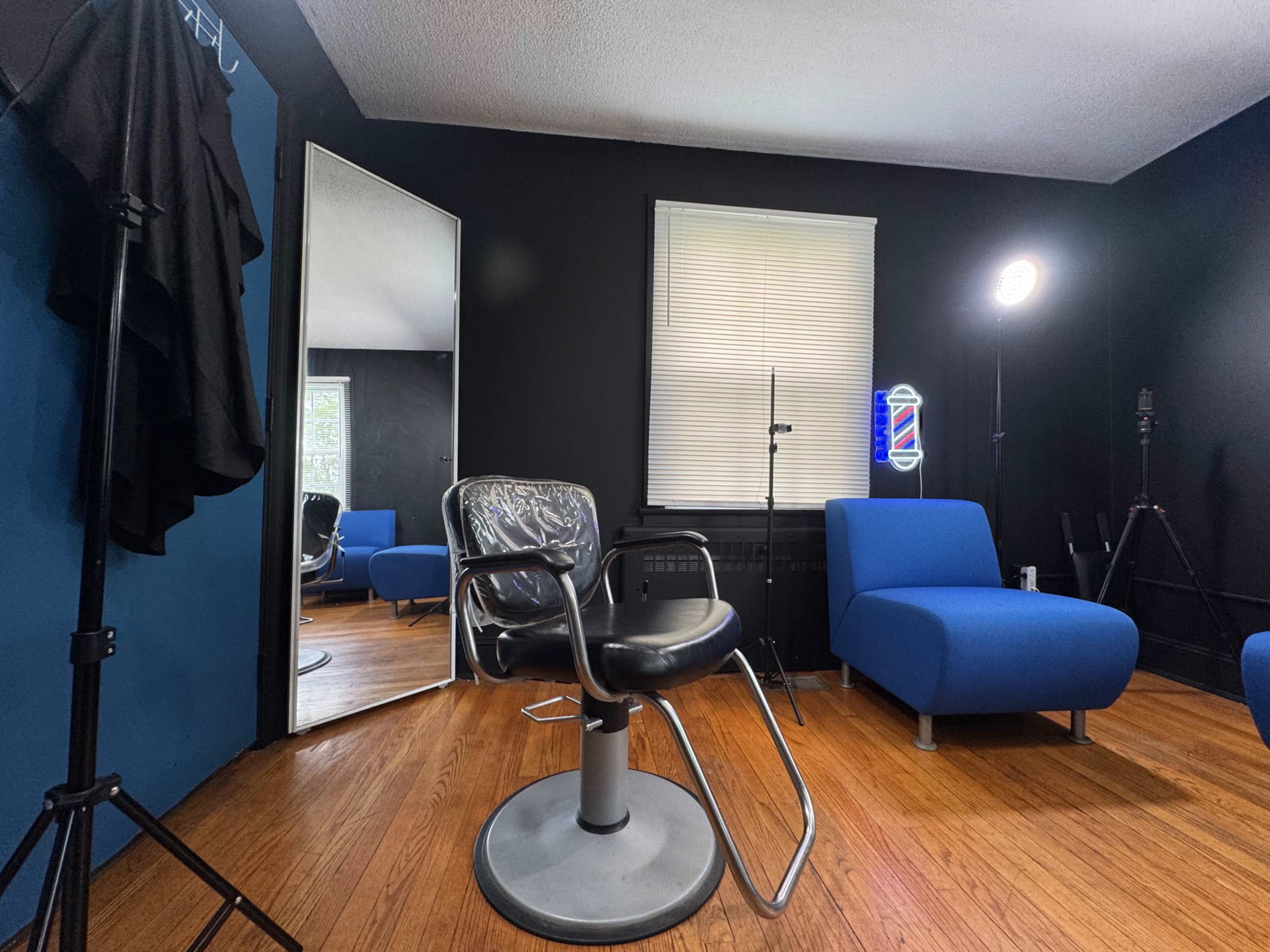 The image shows a barber shop interior featuring a black and blue color scheme, a barber chair, a large mirror, and blue lounge chairs.