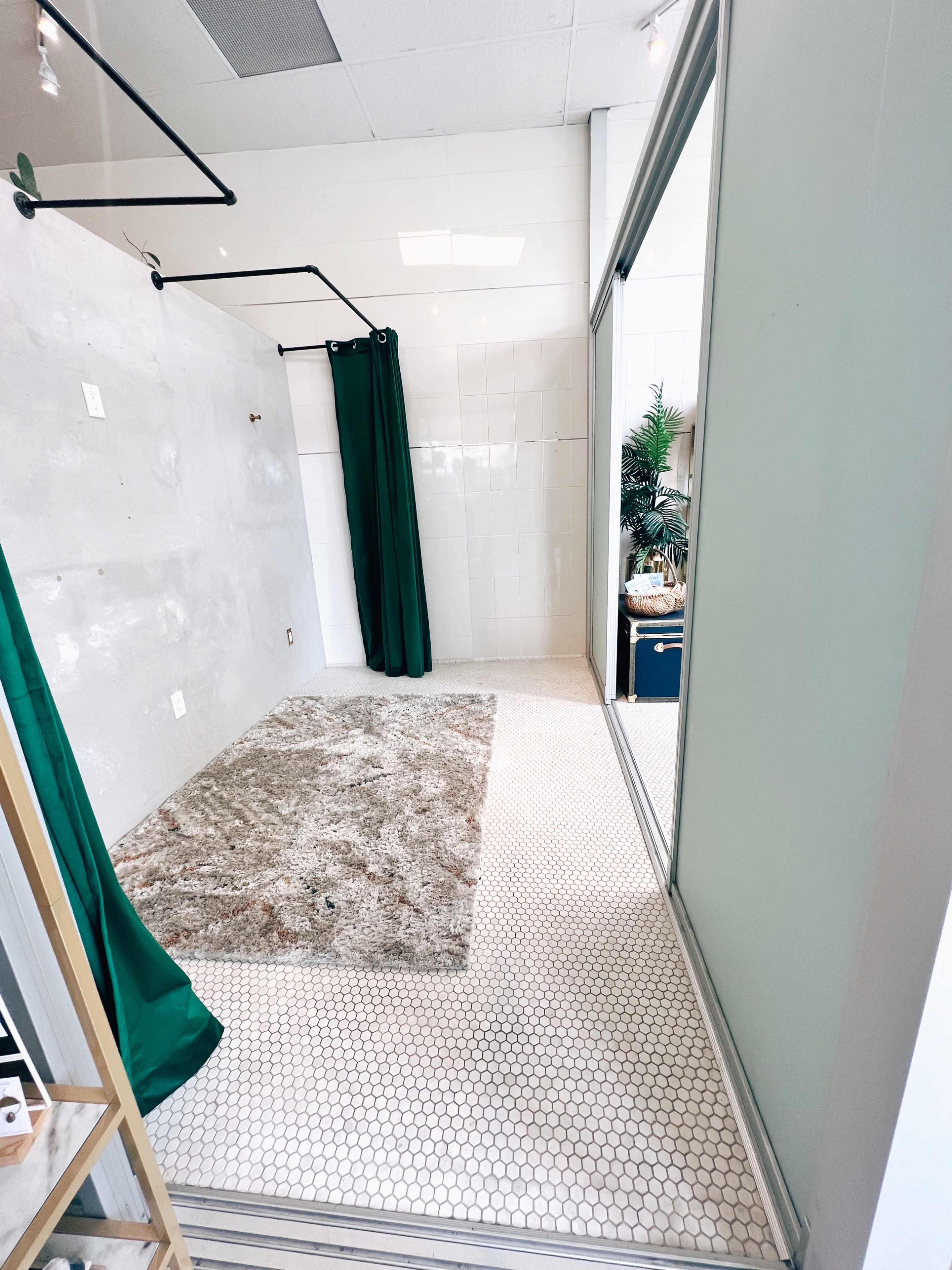 An empty bathroom space with a hexagonal tiled floor, green curtains, and a gray rug on the floor.