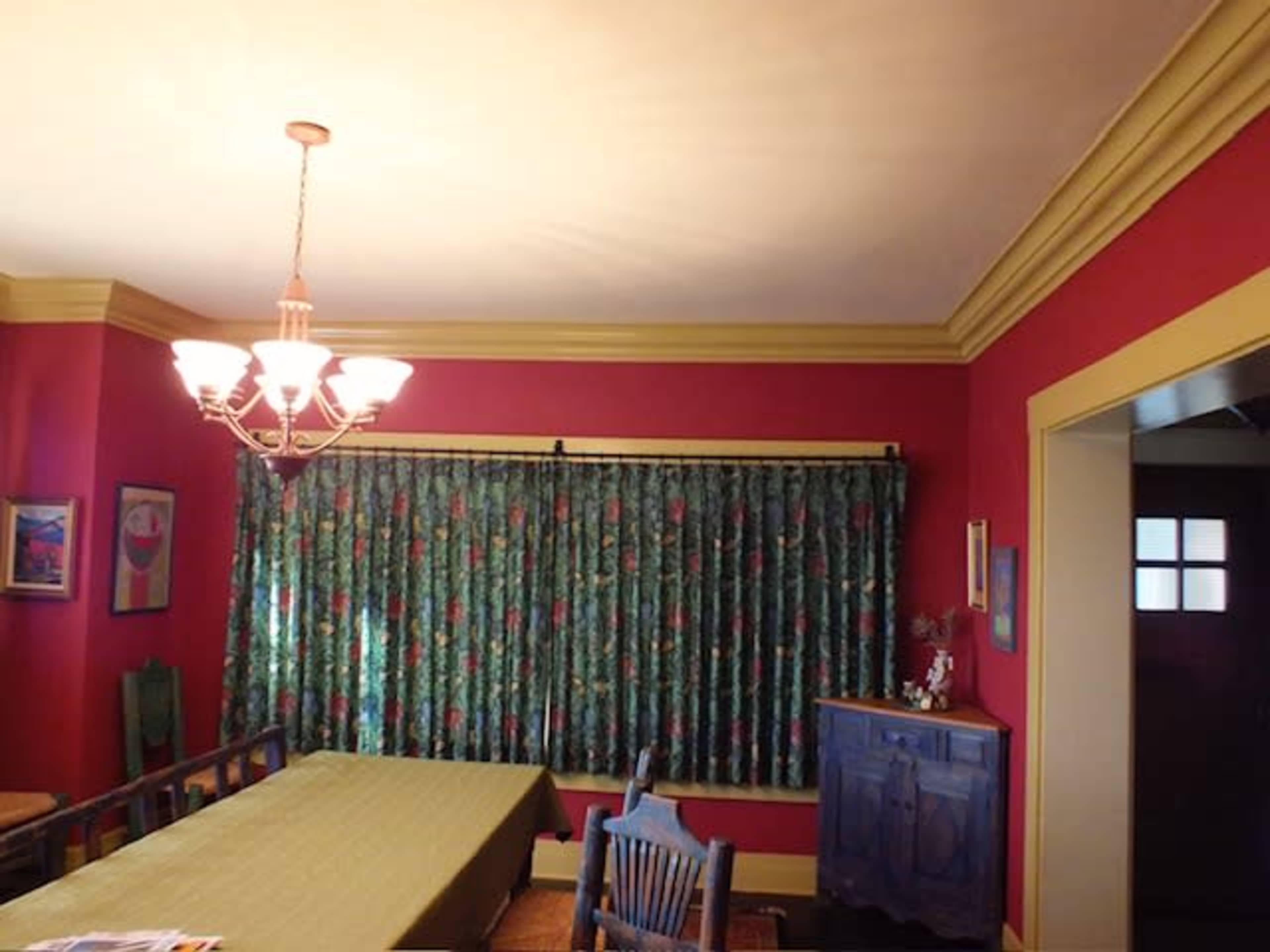 A dining area with a table covered by a green tablecloth, surrounded by floral-patterned curtains, and adorned with a chandelier overhead.