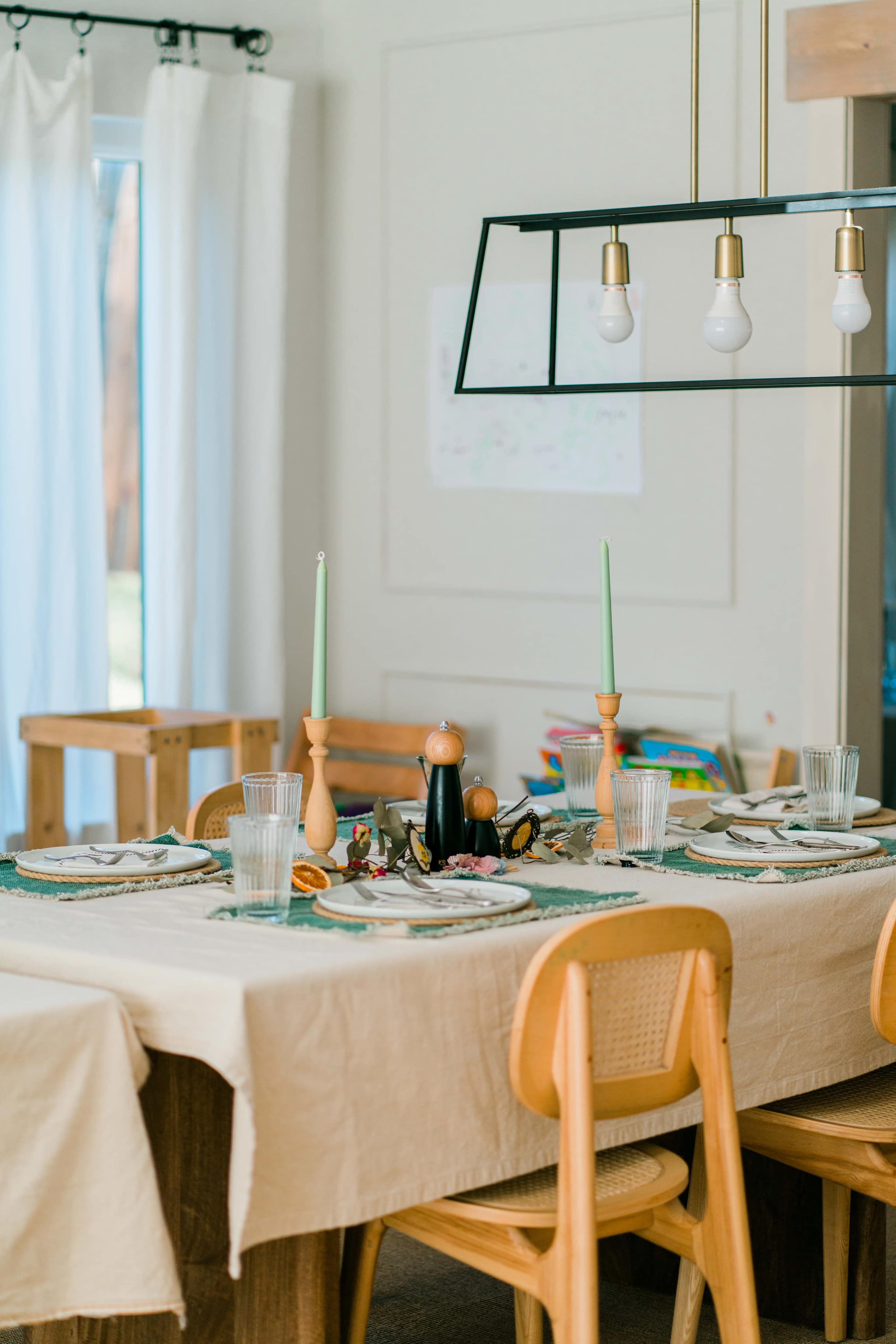 A dining table is set with green candles, glassware, and a tablecloth in a well-lit room.