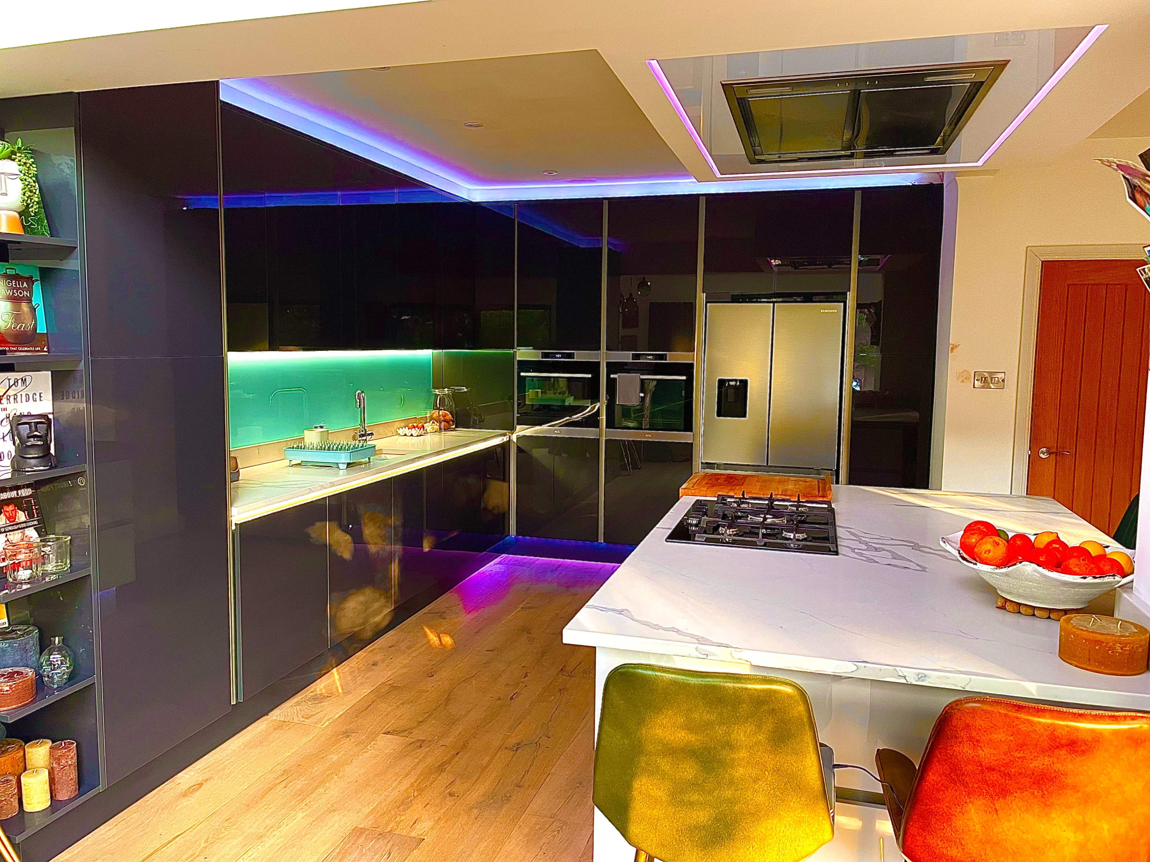 A modern kitchen features sleek cabinets, a large island with colorful chairs, and integrated lighting.