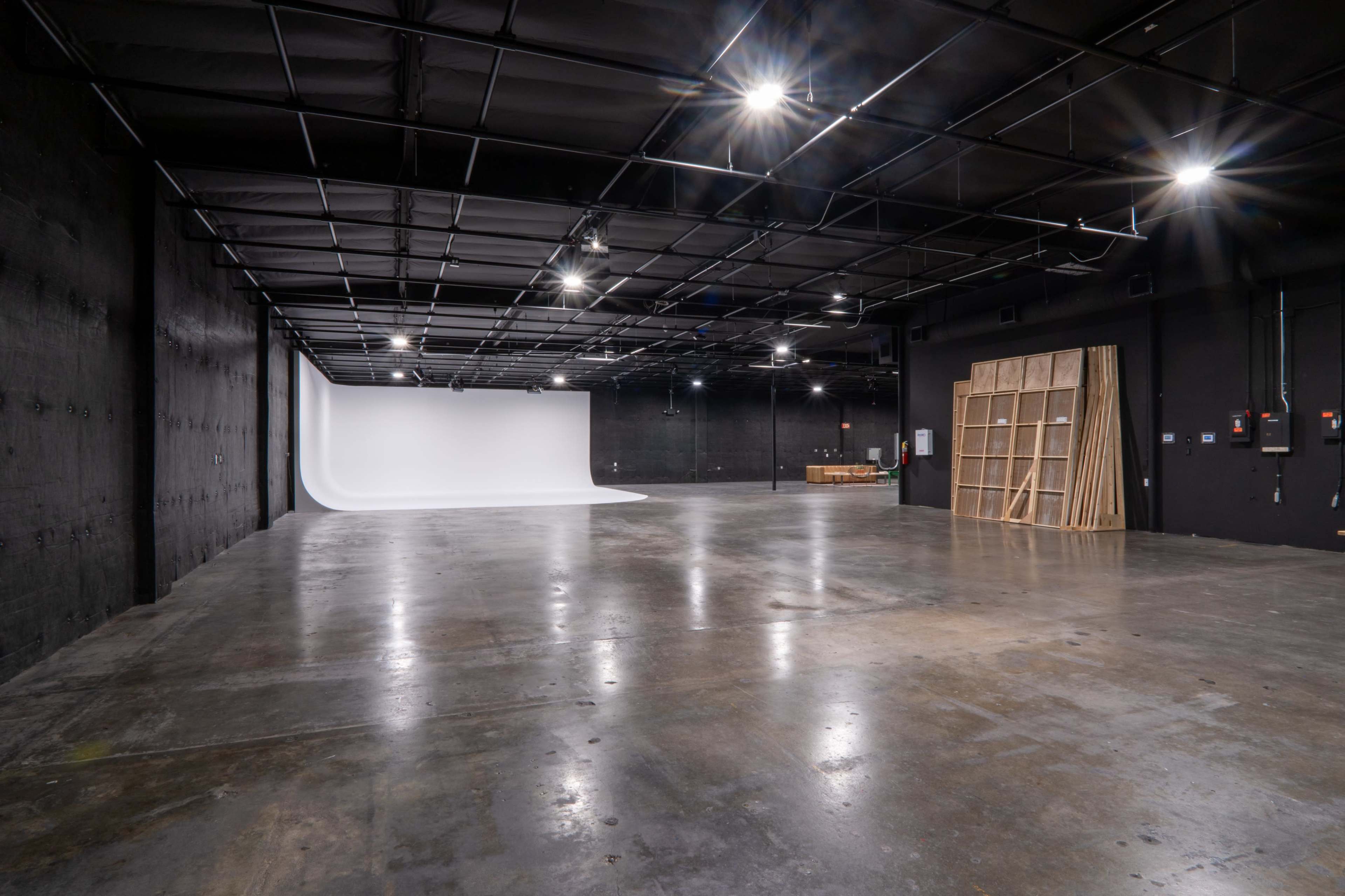A spacious, empty studio with a white backdrop and dark walls, illuminated by overhead lights.