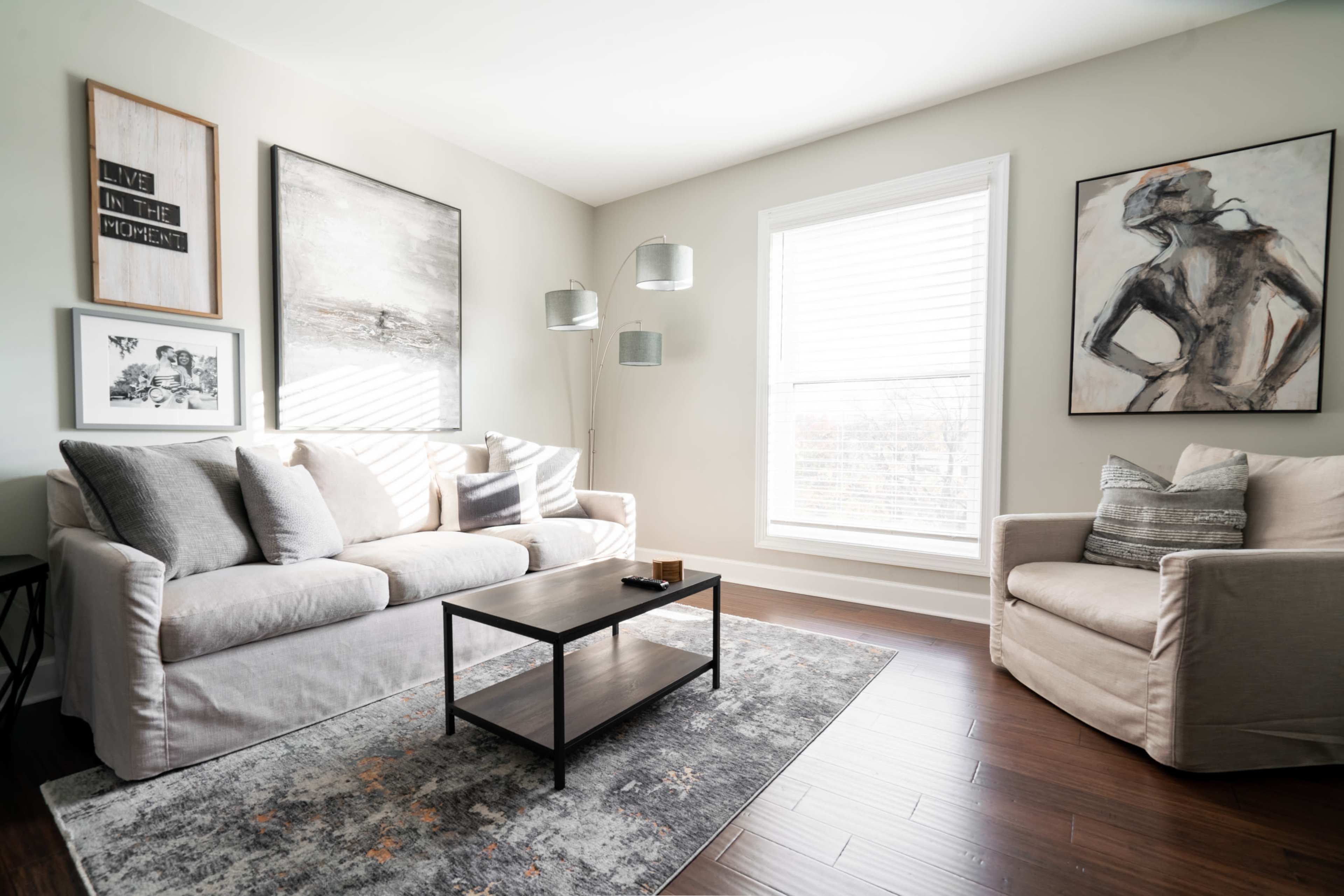 The living room features a light-colored sofa, an armchair, a coffee table, and several framed artworks on the walls.