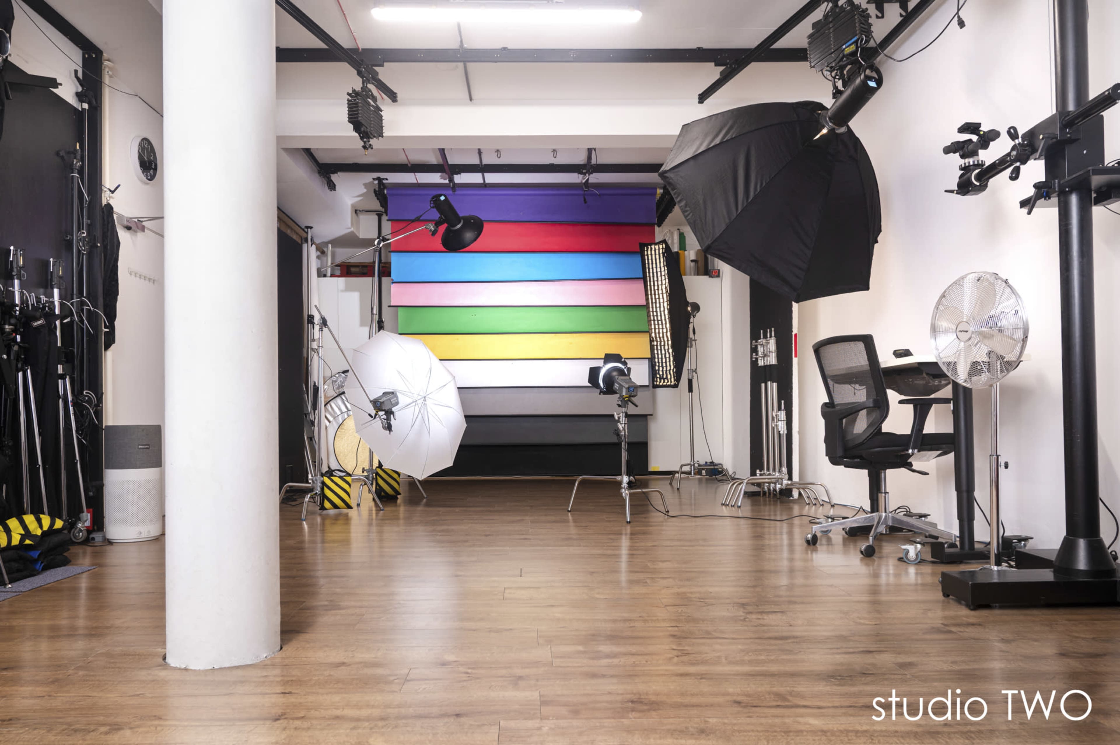 The image shows a photography studio with colorful backdrops, lighting equipment, and a chair arranged in an open space.