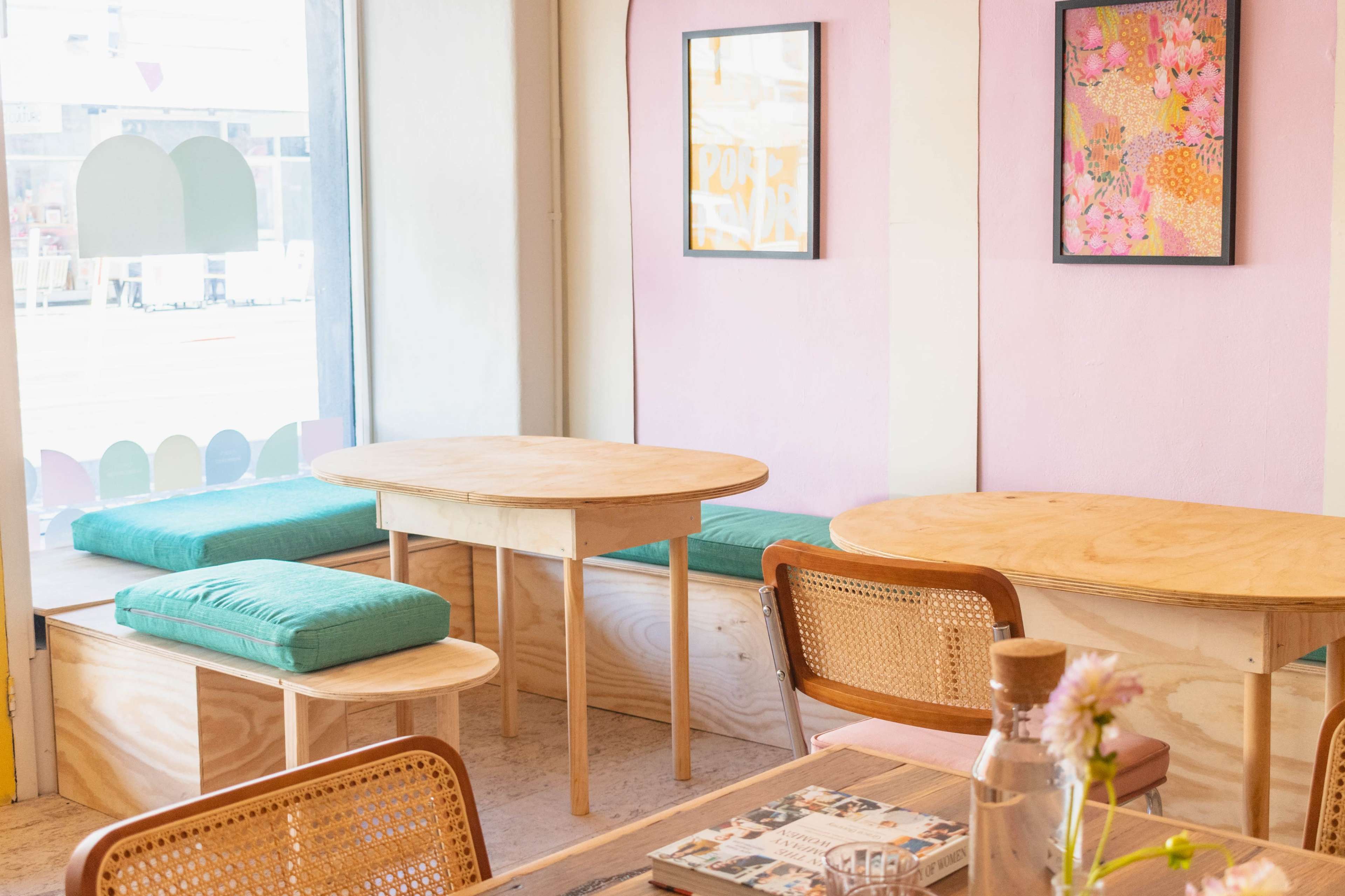 A bright cafe interior with wooden tables, cushioned seating, and colorful wall art.