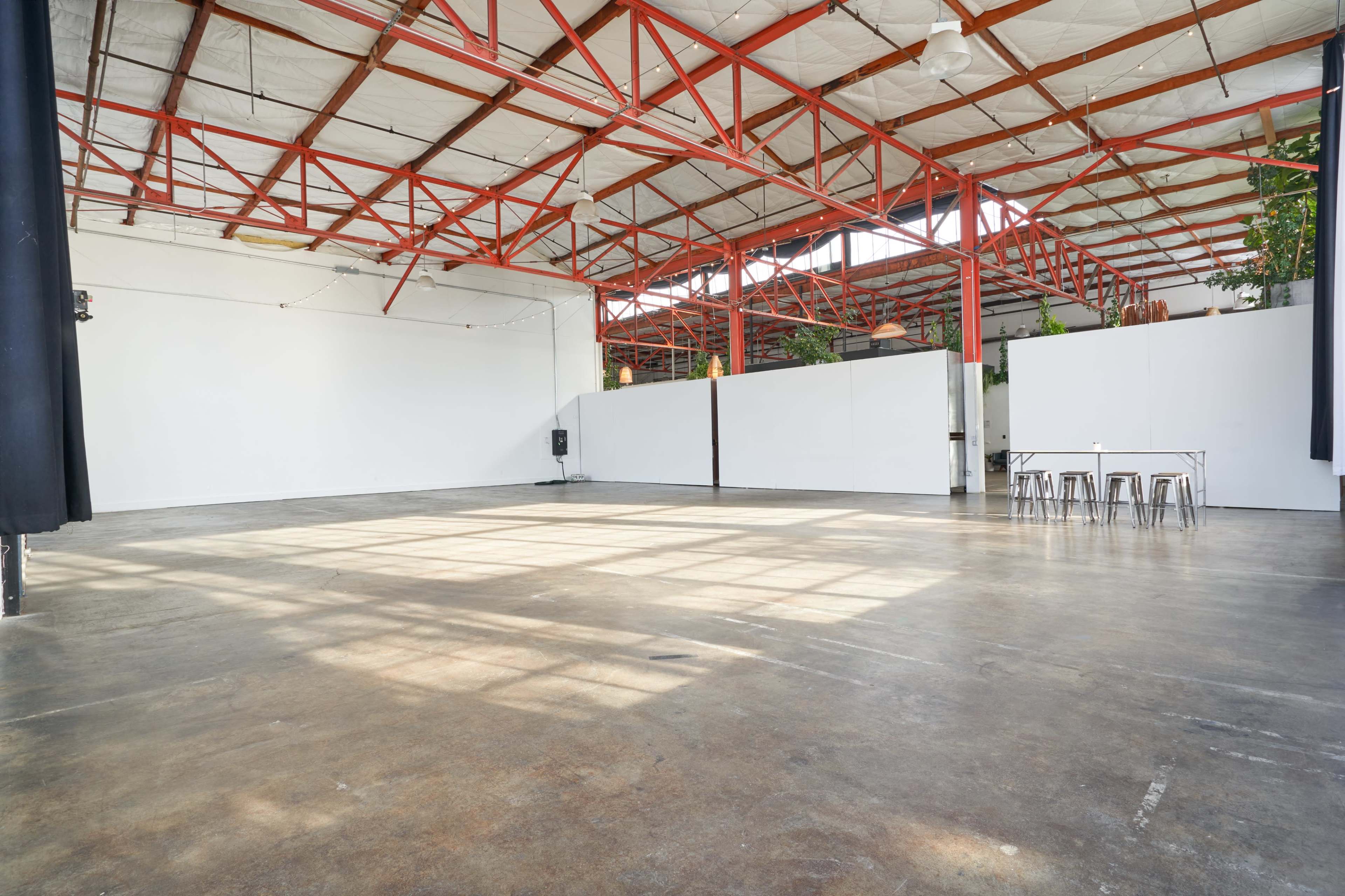 A spacious, industrial-style room with high ceilings, large windows, and empty concrete floors.