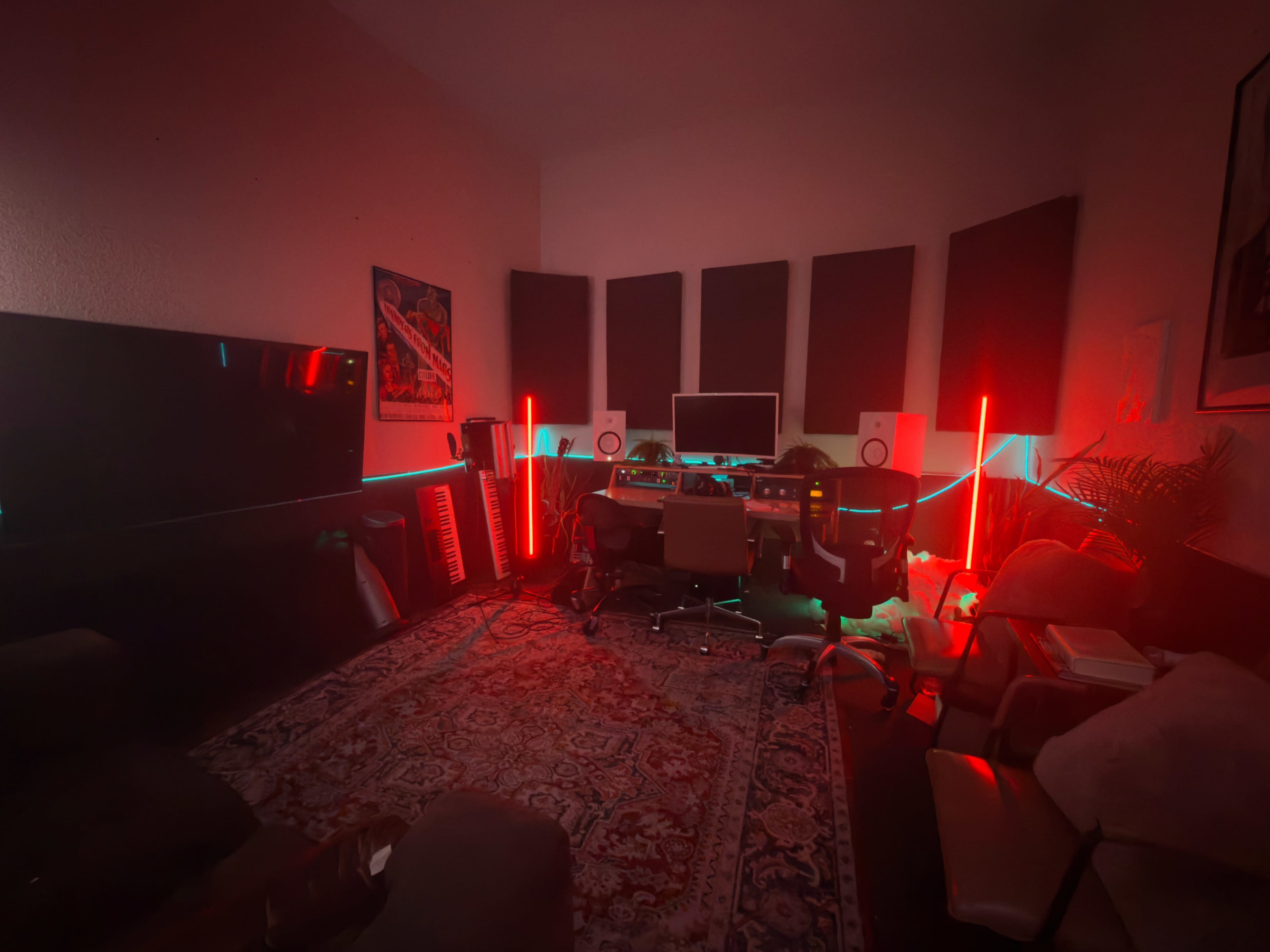 The image shows a dimly lit music studio with acoustic panels, a mixing console, colorful LED lights, and various instruments arranged around the space.