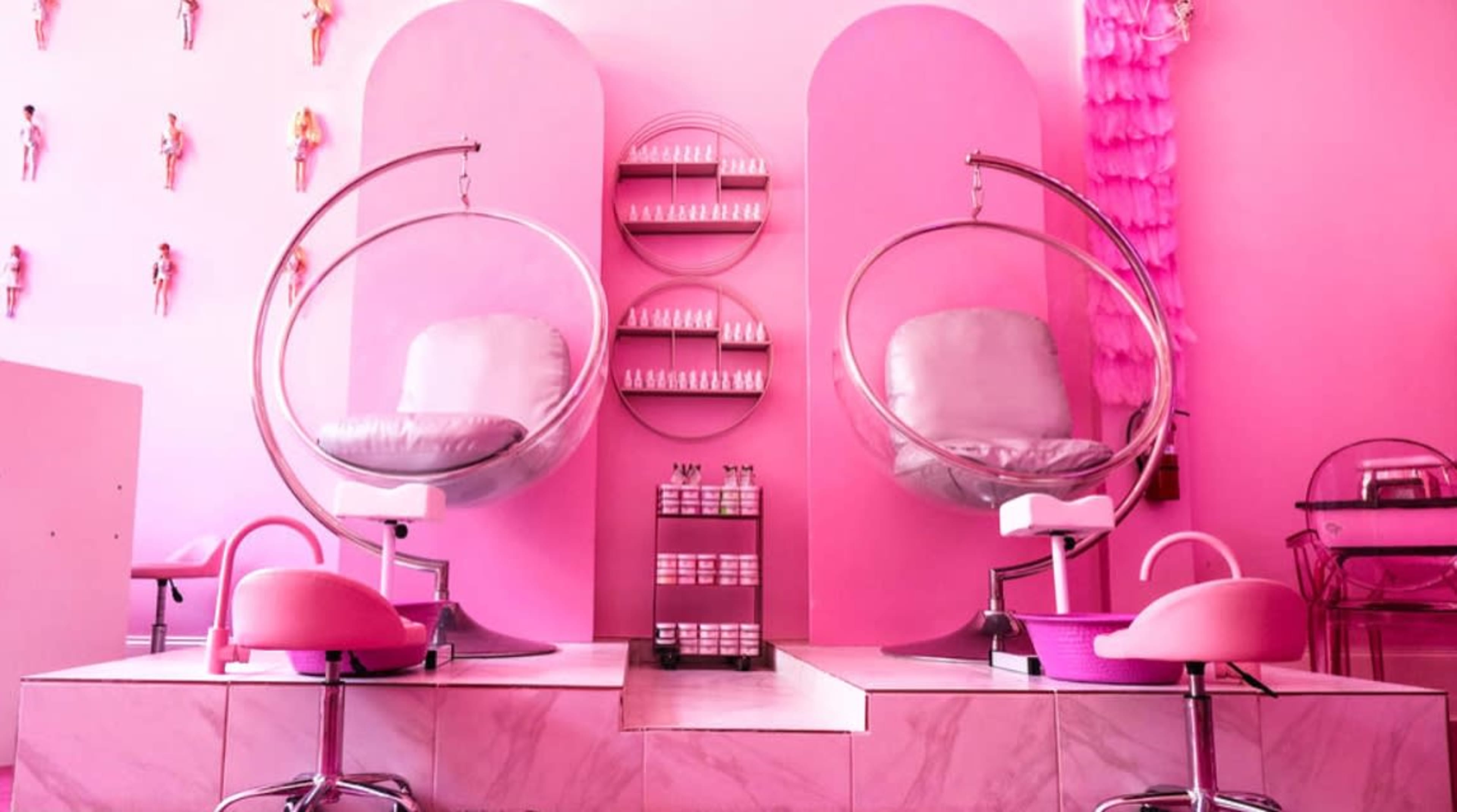 A pink-themed beauty salon with two elegant pedicure chairs, round mirrors, and a display of products on the wall.