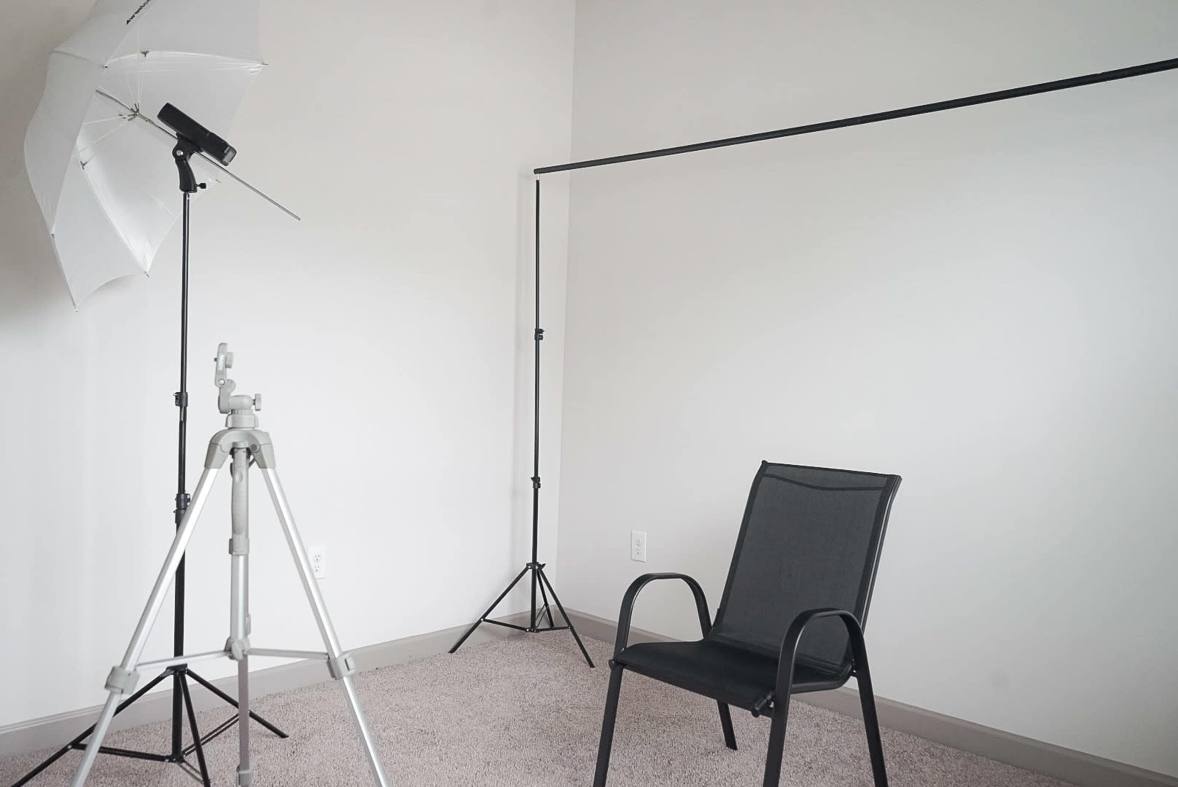 A minimalistic studio setup with a black chair positioned on carpet, accompanied by a lighting umbrella and a backdrop stand.