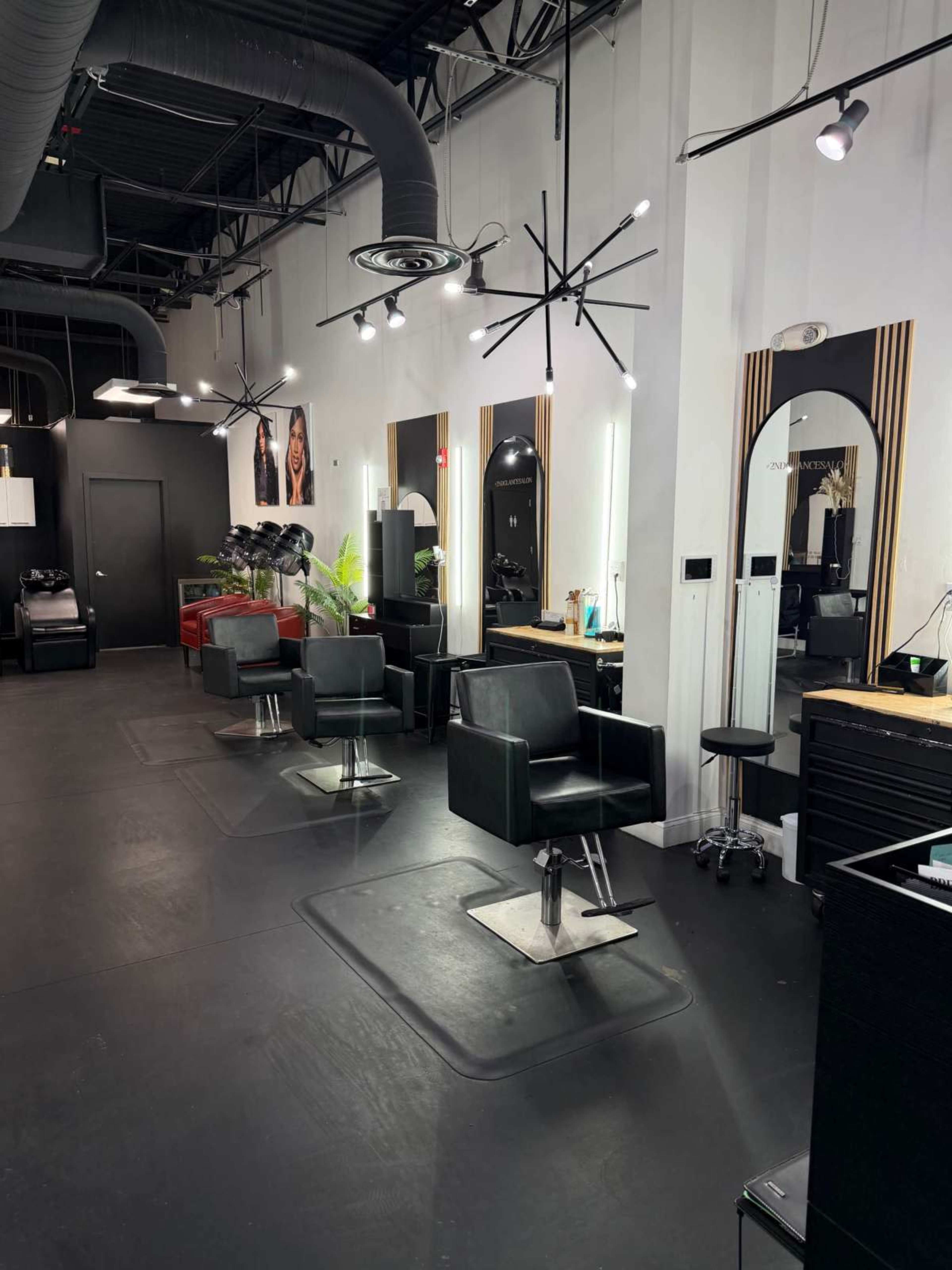 The image shows a modern hair salon interior with black styling chairs, mirrors, and minimalist lighting fixtures.