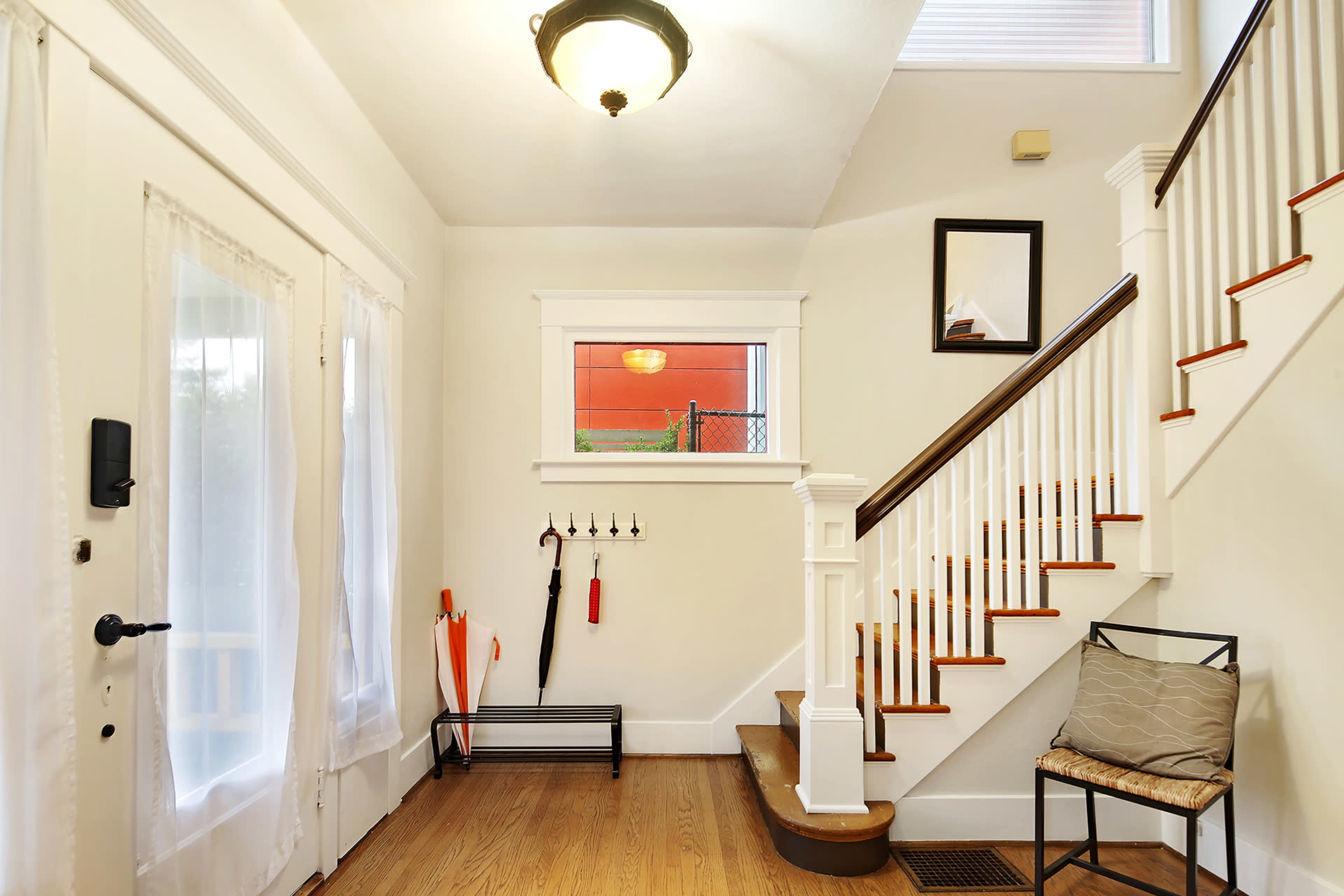 A well-lit entryway featuring a staircase, a small chair, and an umbrella stand beside a set of double doors with sheer white curtains.