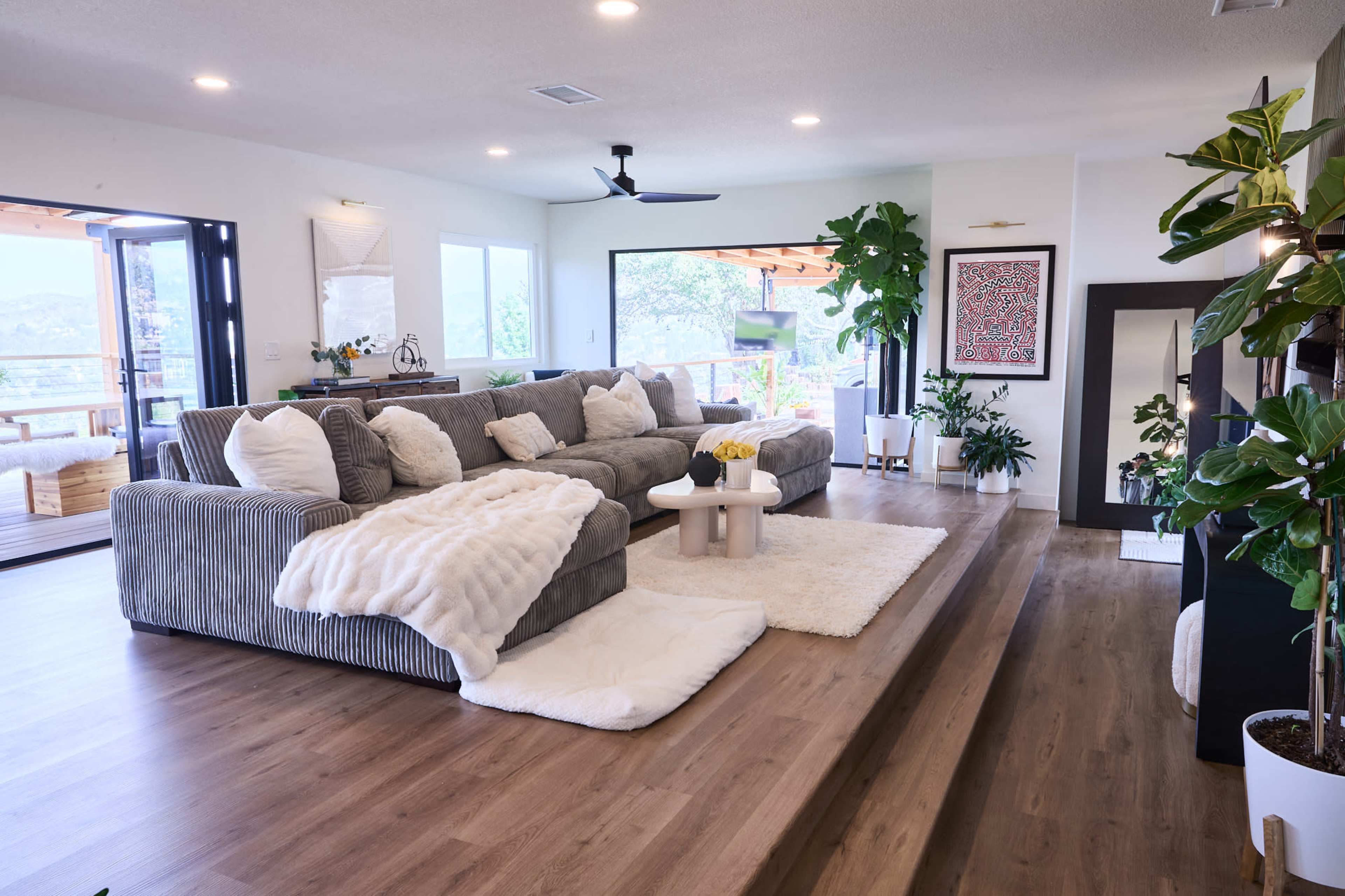 A contemporary living room with a gray sectional sofa, a round white coffee table, and large windows providing a view of the outdoors.
