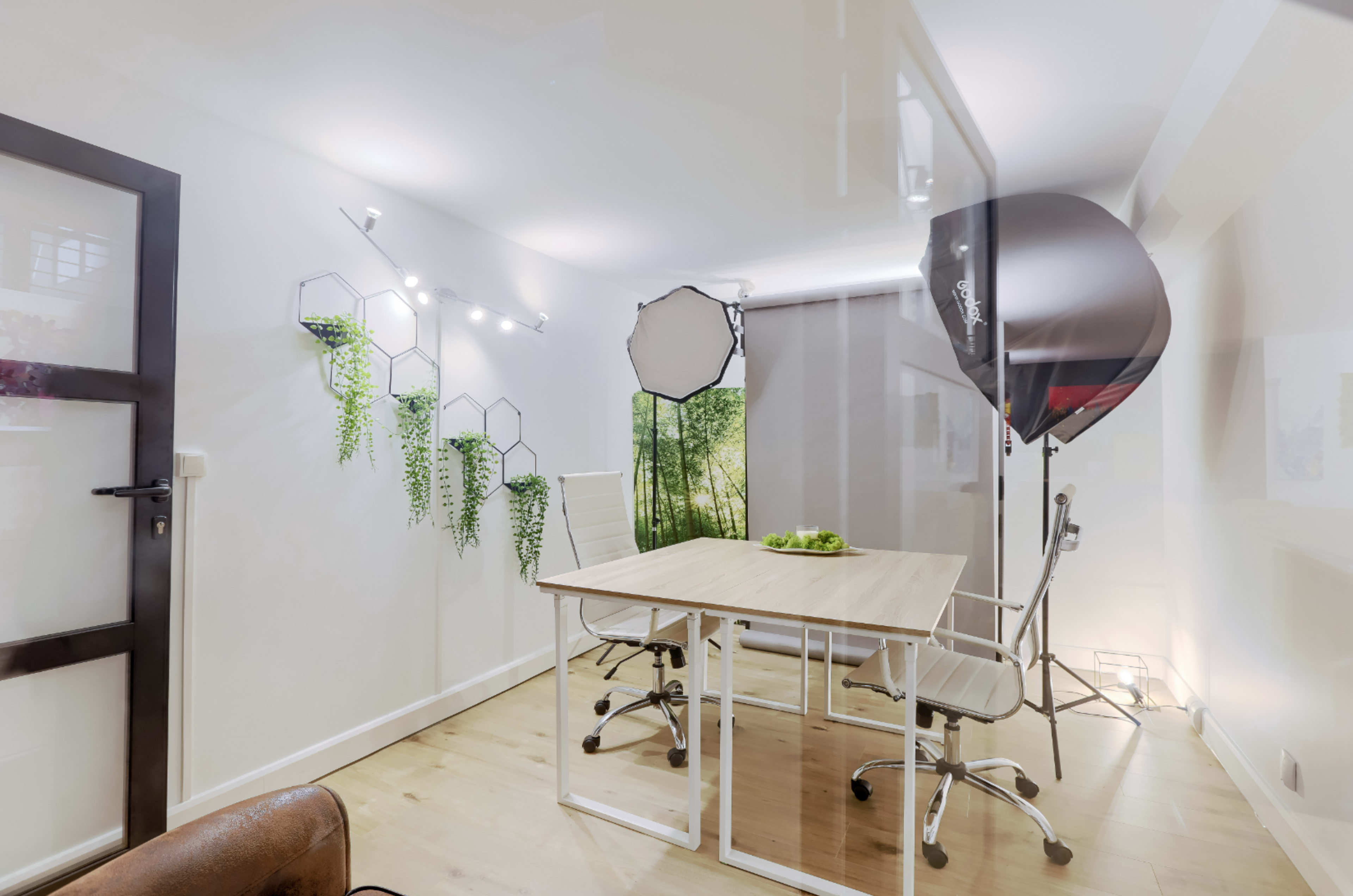 A well-lit, minimalist office space featuring a wooden table, two chairs, and a backdrop of greenery on one wall.