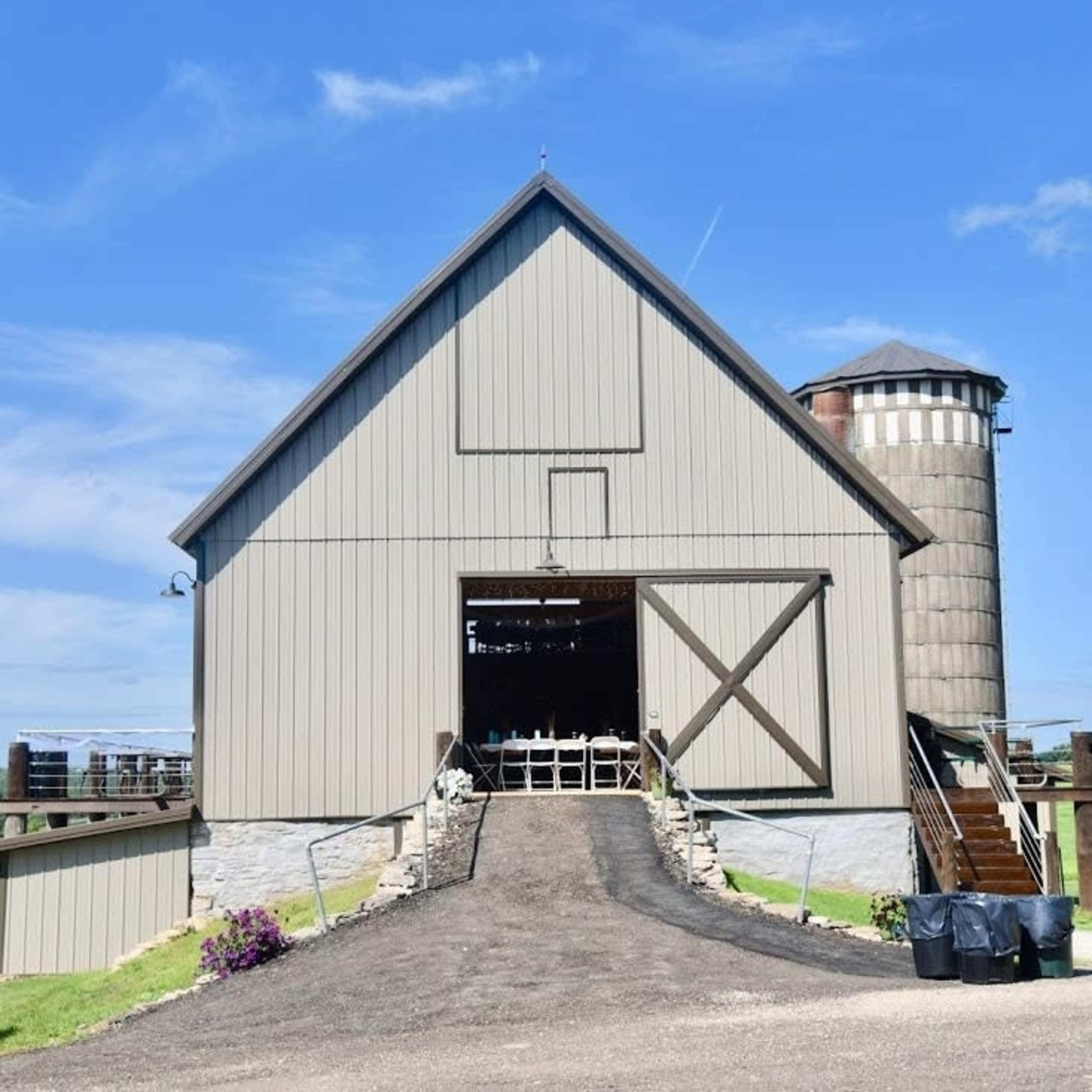 The image shows a large, gray barn with a silo beside it, set against a clear blue sky.