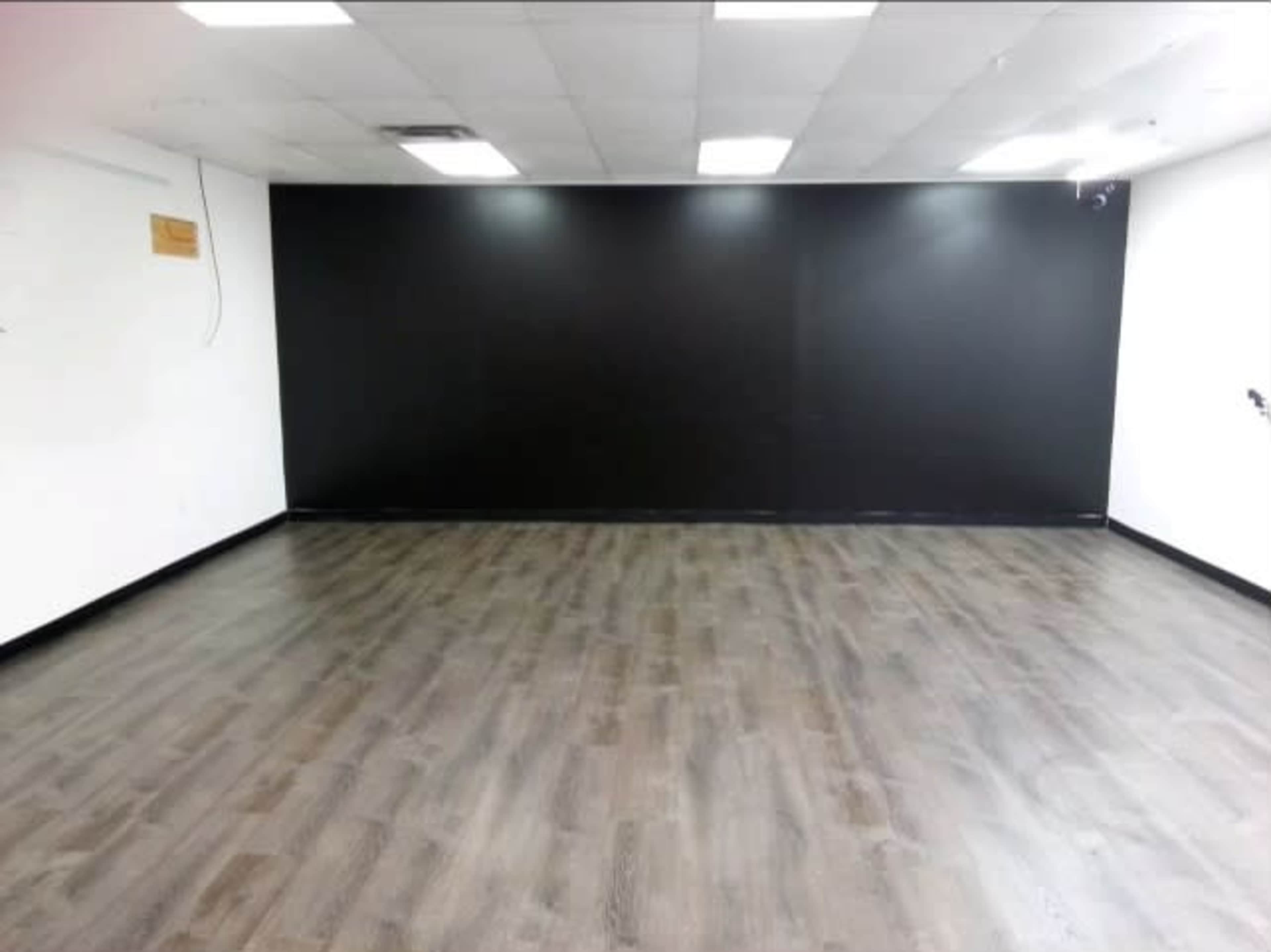 The image shows a spacious, empty room with a dark wall and wooden flooring.