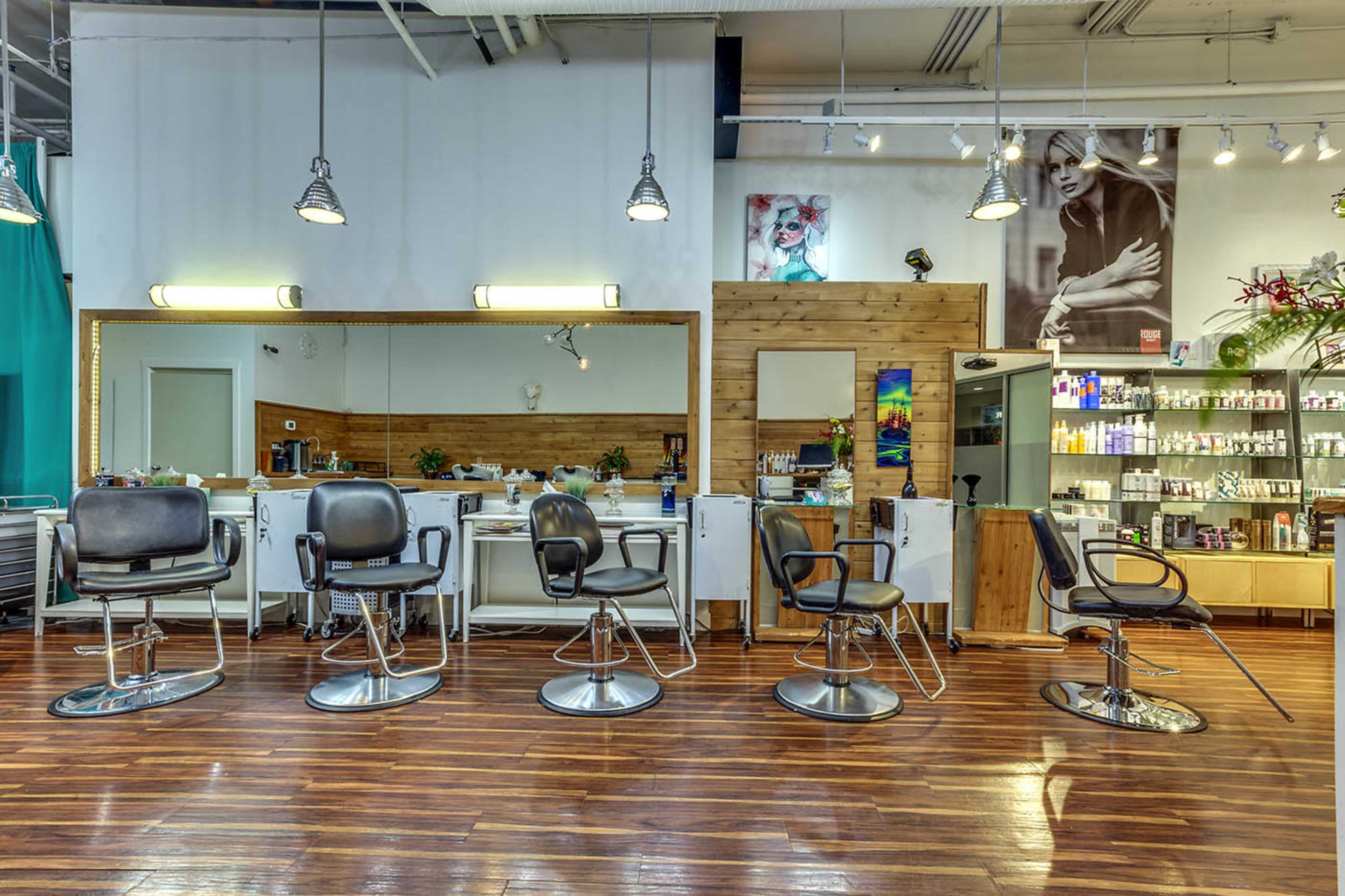A modern hair salon with five styling chairs, large mirrors, and a display of hair products along the back wall.