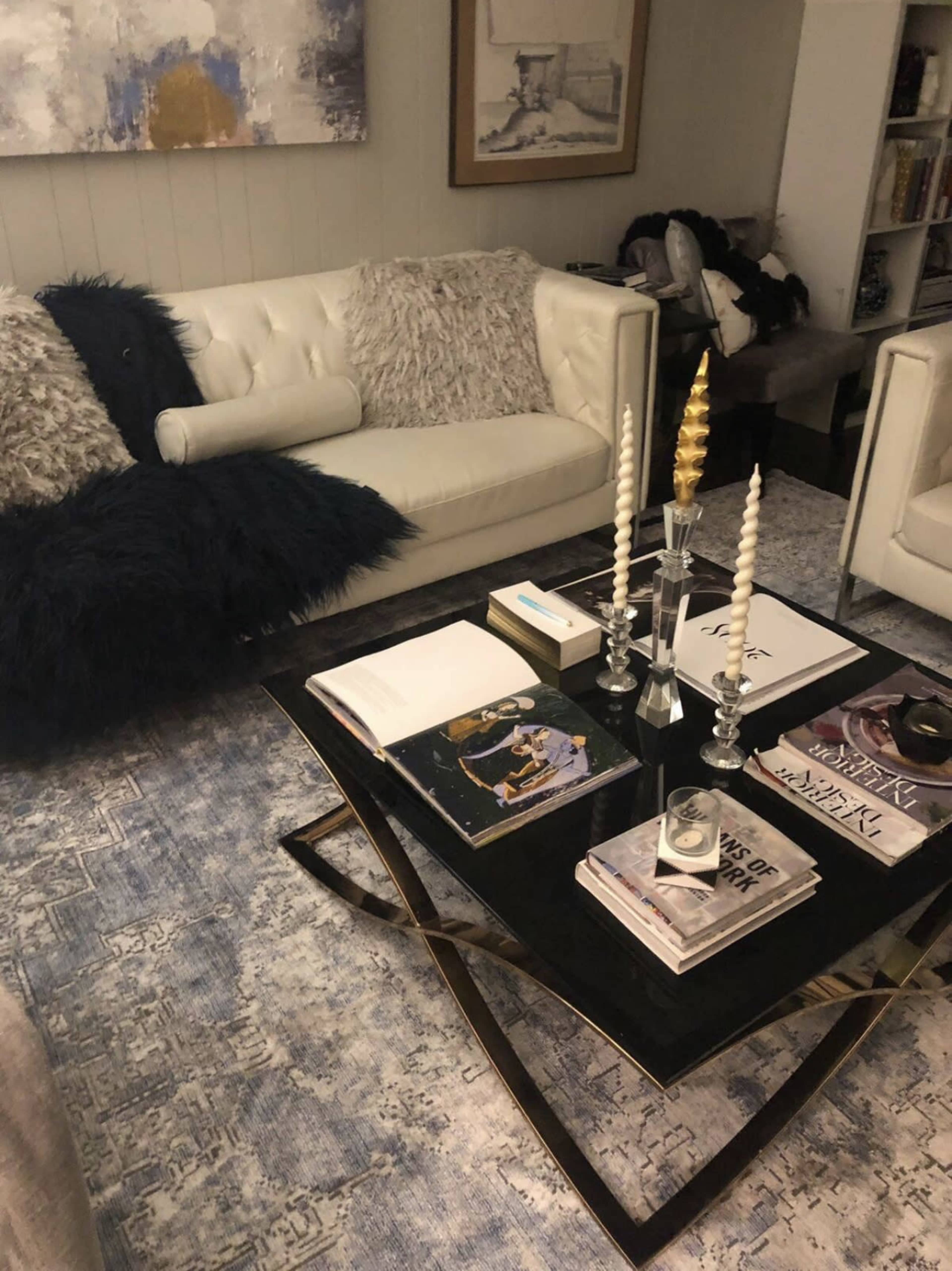 The image shows a modern living room with a white sofa, a coffee table adorned with art books and decorative items, and a large area rug.