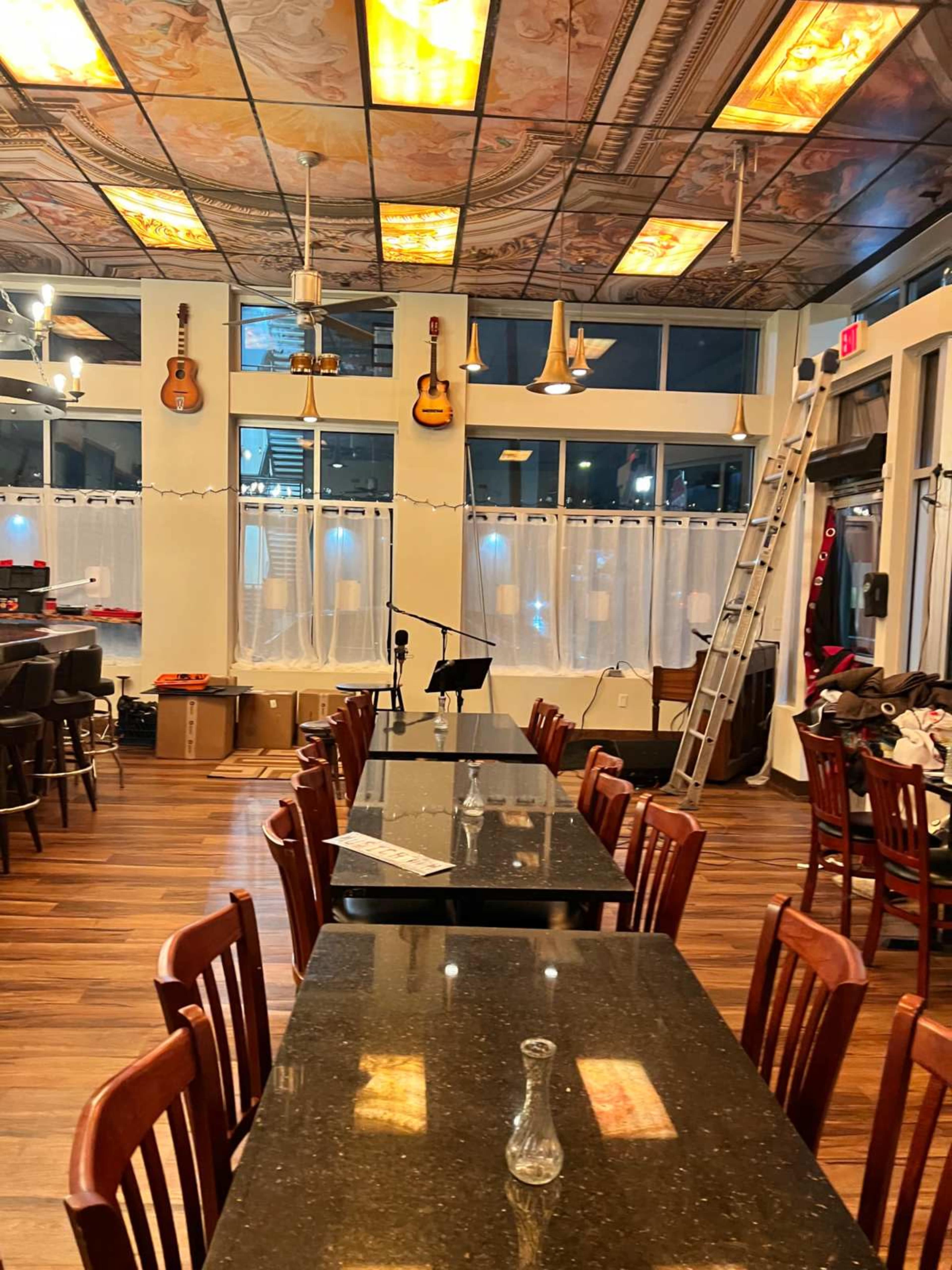 The image shows an empty restaurant interior featuring long dark tables, wooden chairs, and a musical theme with guitars hanging on the walls.