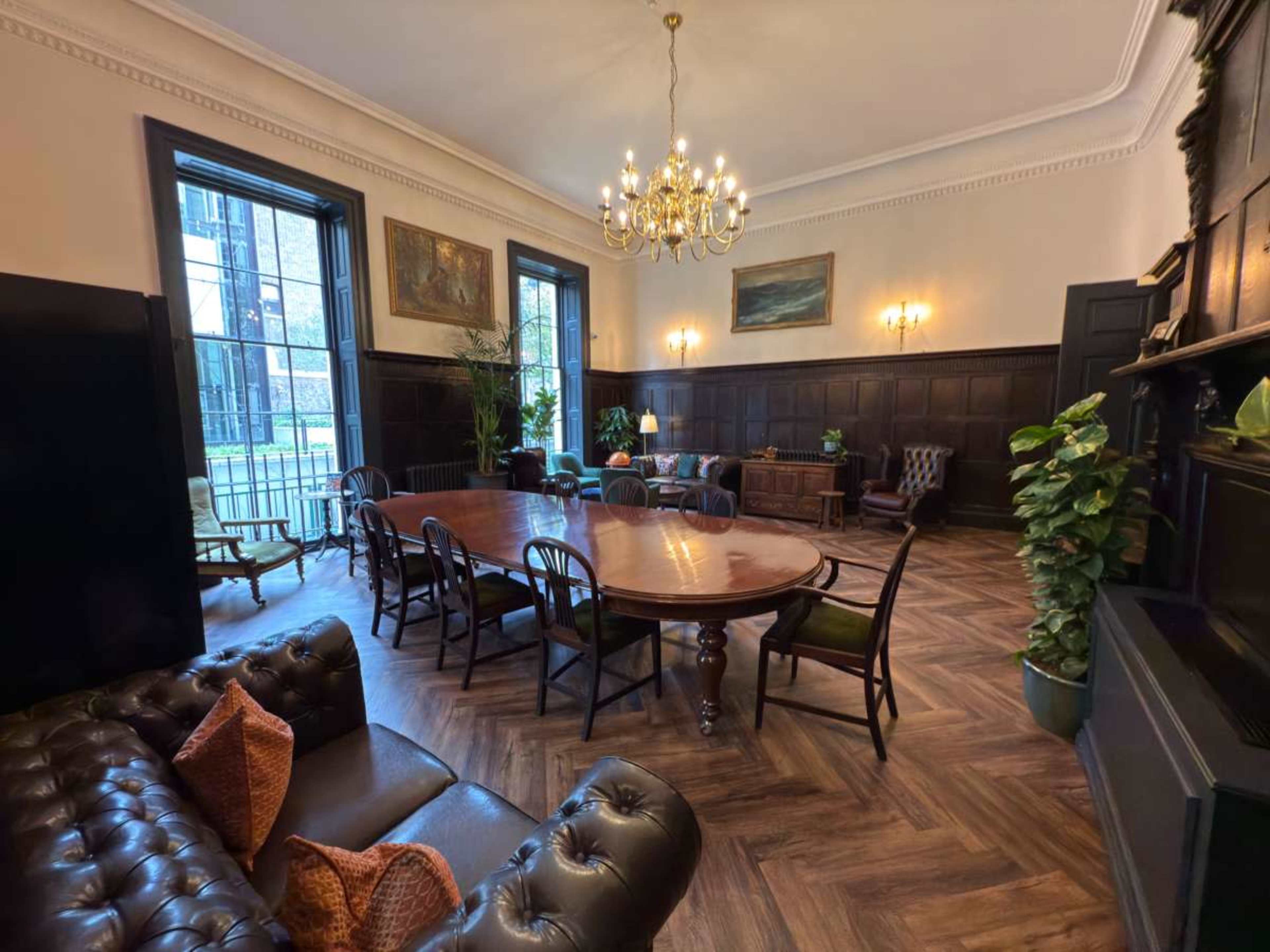 The room features a large wooden table surrounded by chairs, with a chandelier overhead and dark wood paneling on the walls.