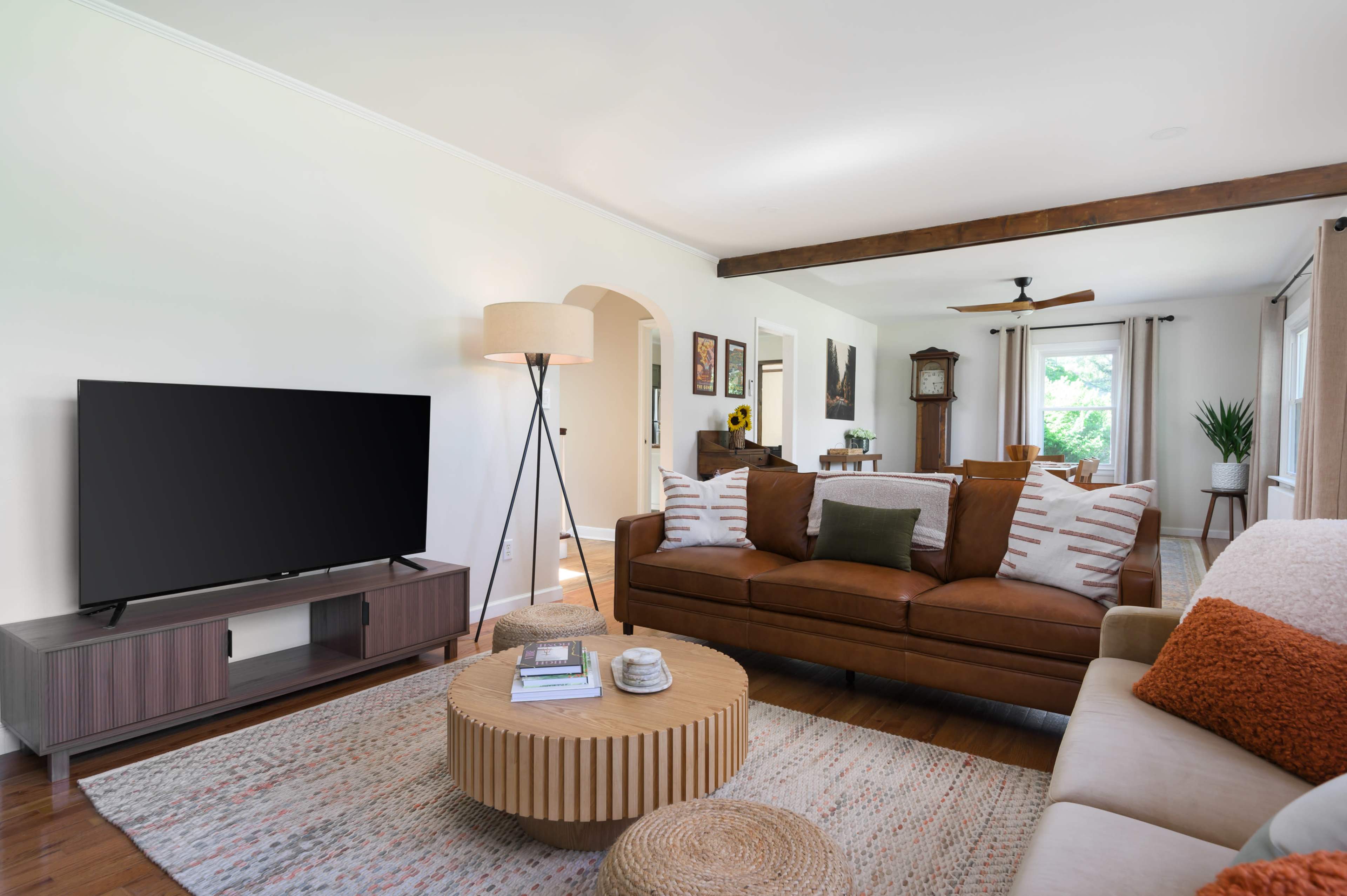 The living room features a brown leather sofa, a circular coffee table, a large TV stand, and a mix of decorative elements against a light-colored wall.